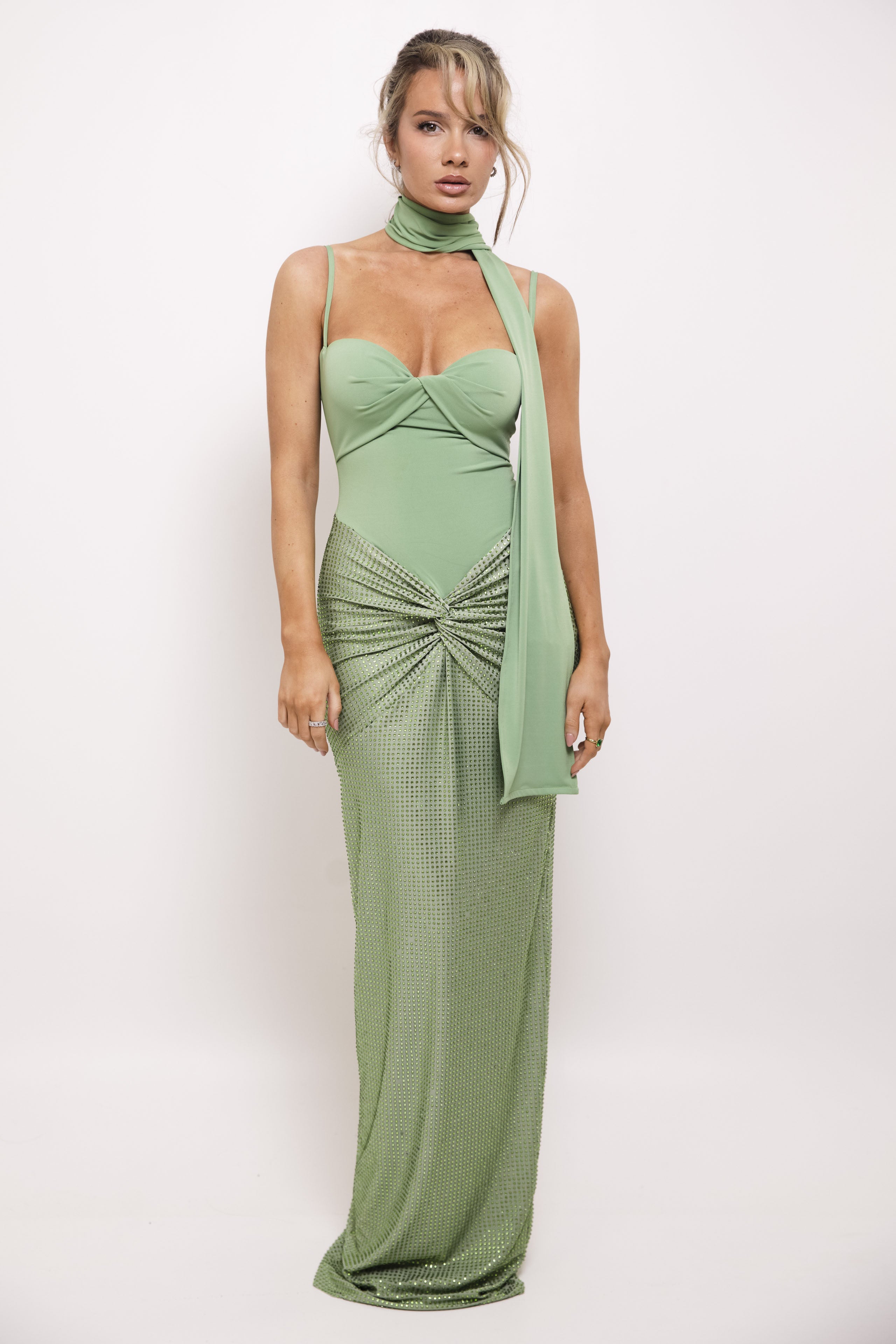 Elegant floor-length dress in soft green with intricate sequined draping and a stylish accessory scarf.