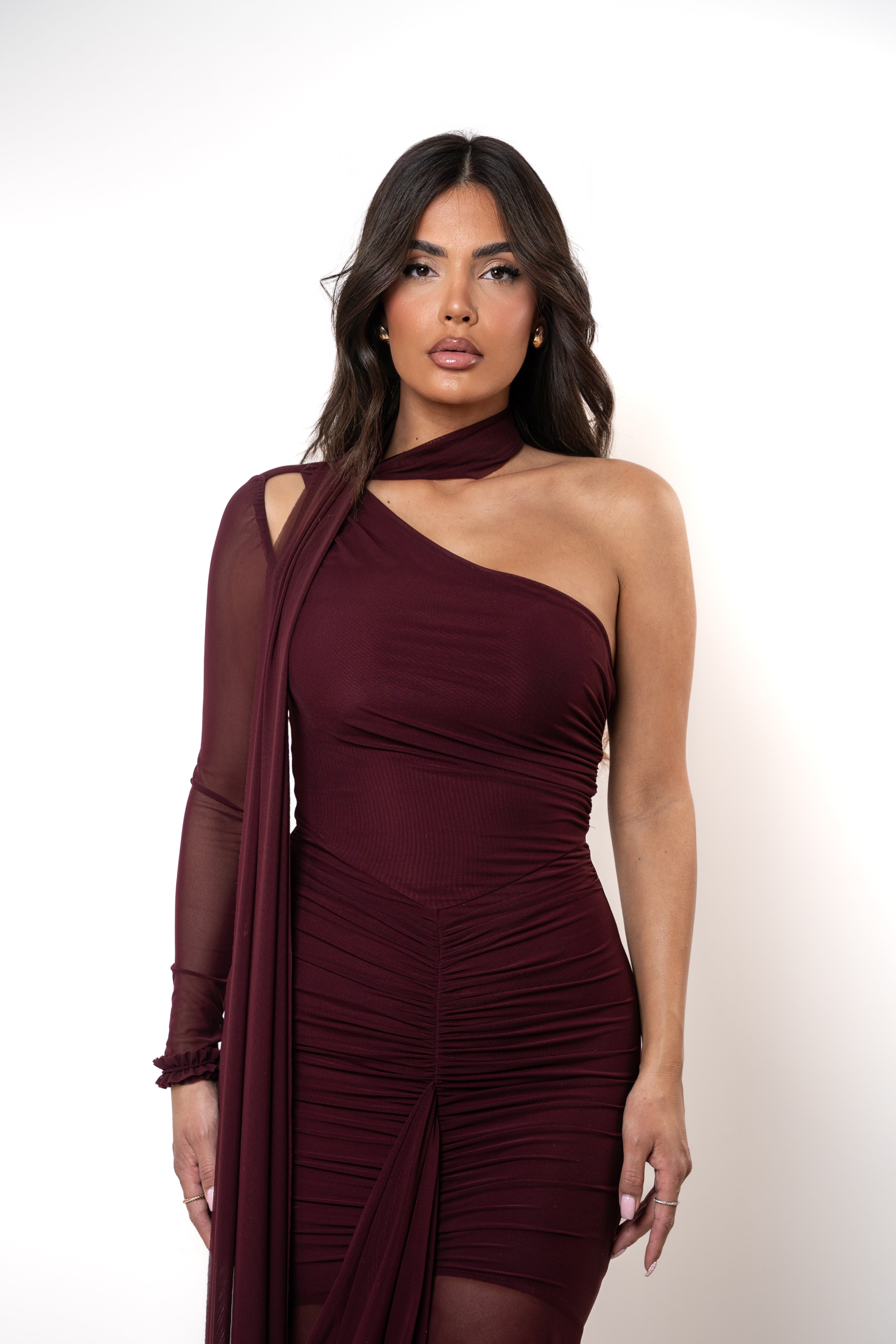 Woman wearing a burgundy one-shoulder dress with a sheer overlay on a white background