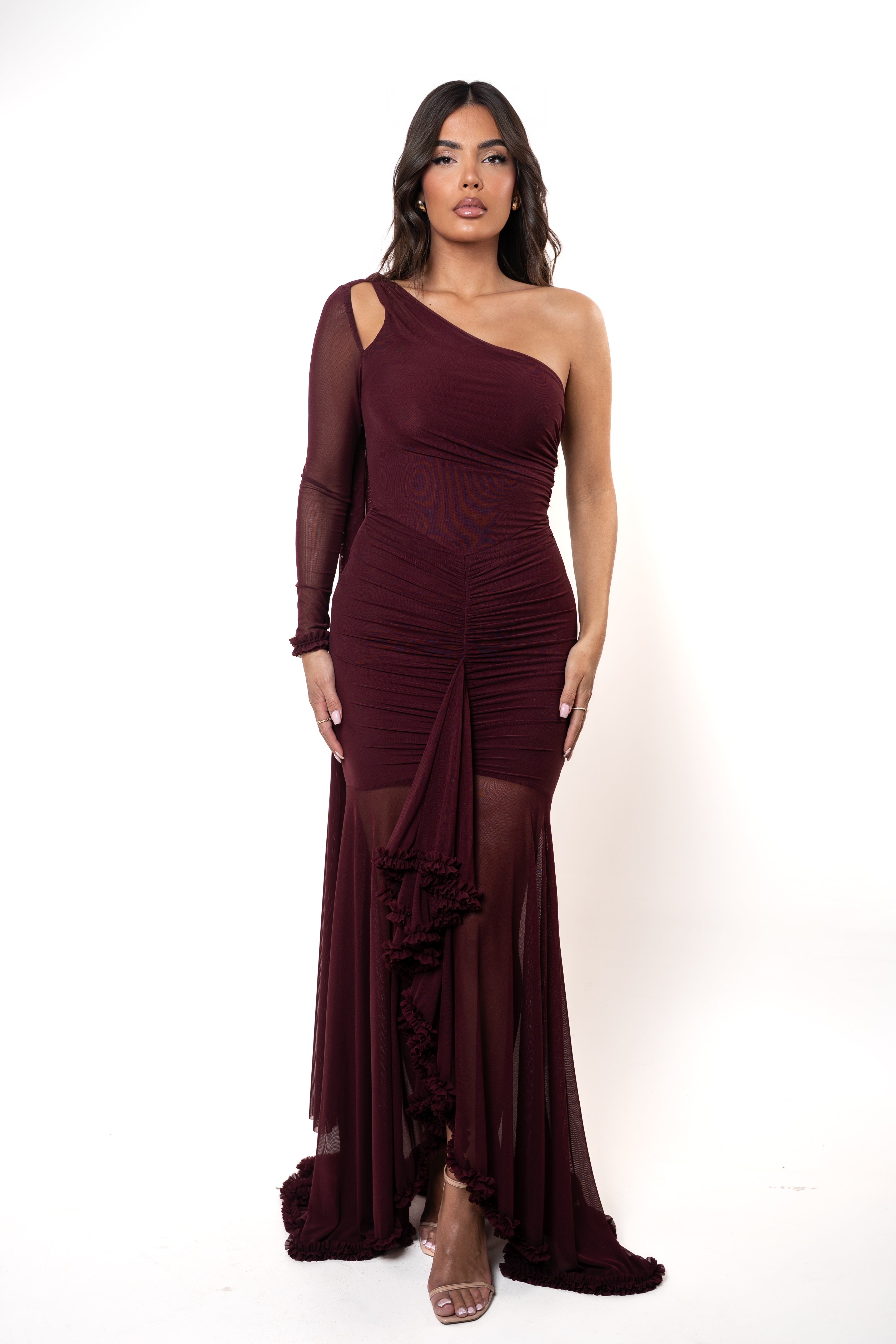 Woman wearing a burgundy one-shoulder dress with sheer sleeves on a white background