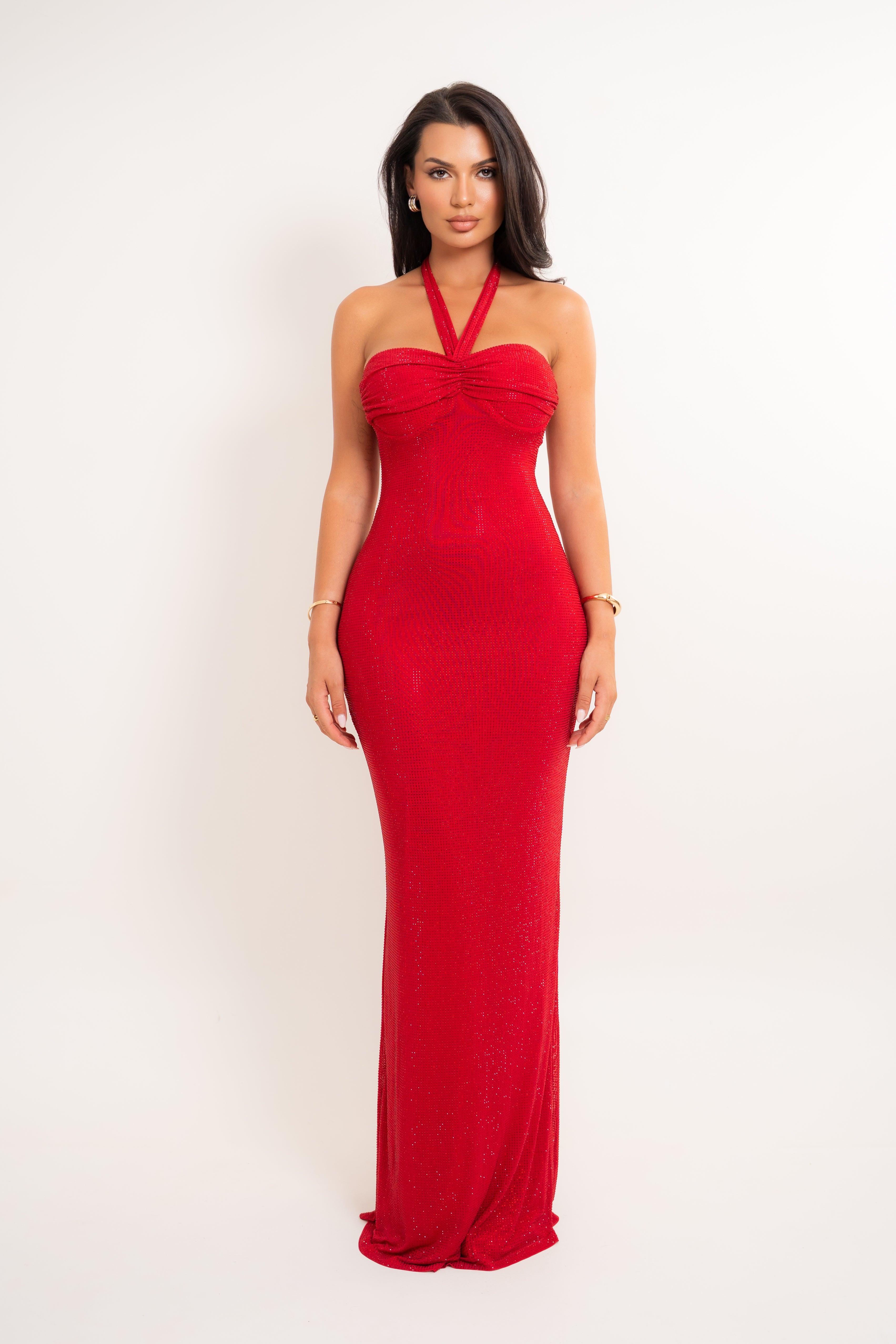 A woman modeling a bright red halter-neck maxi dress with a ruched sweetheart bodice, photographed against a plain white studio background.