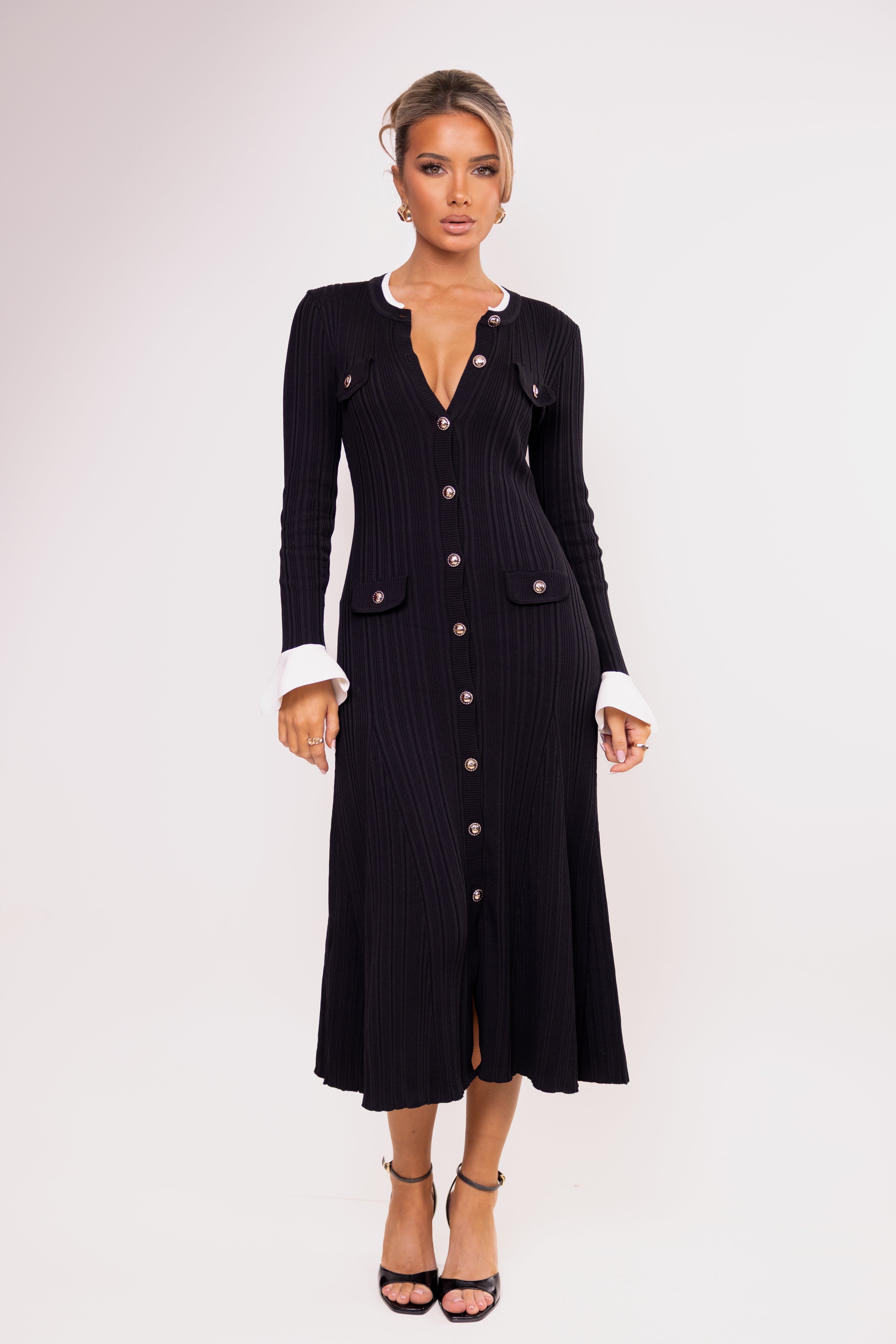 Woman wearing a black ribbed dress with buttons on a white background