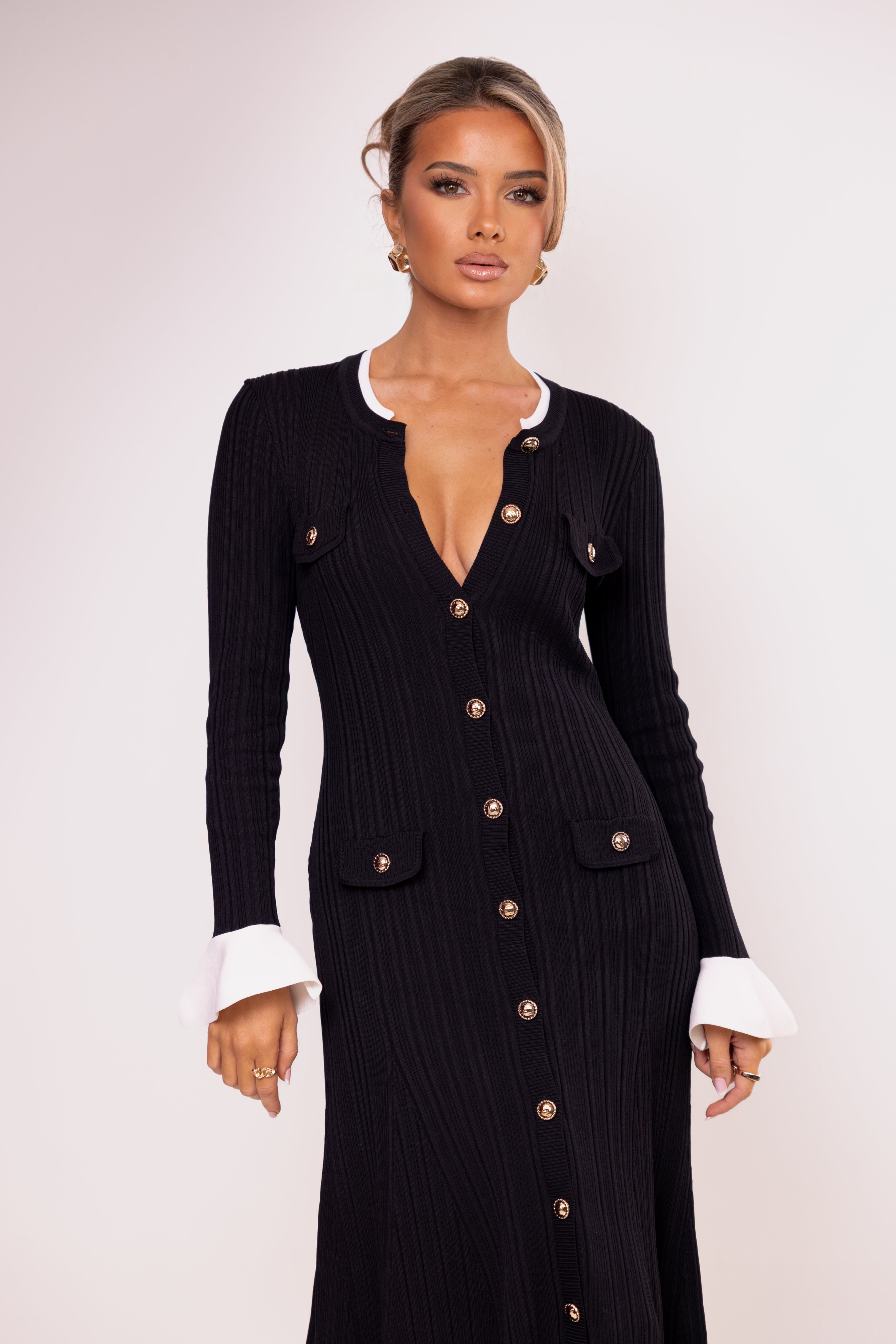 Woman wearing a black ribbed cardigan with gold buttons on a white background