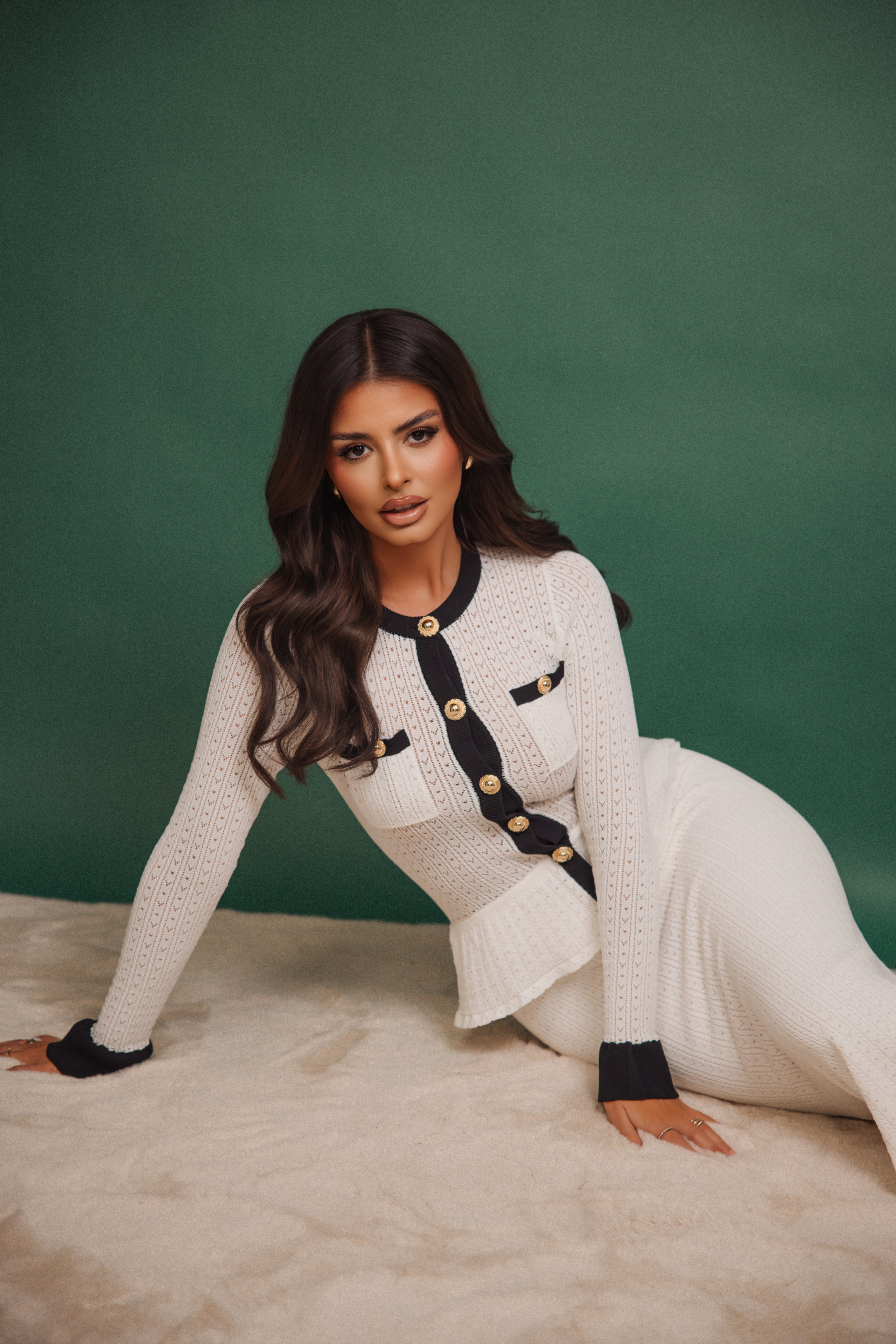 Woman in a white and black outfit sitting on a textured surface with a green background