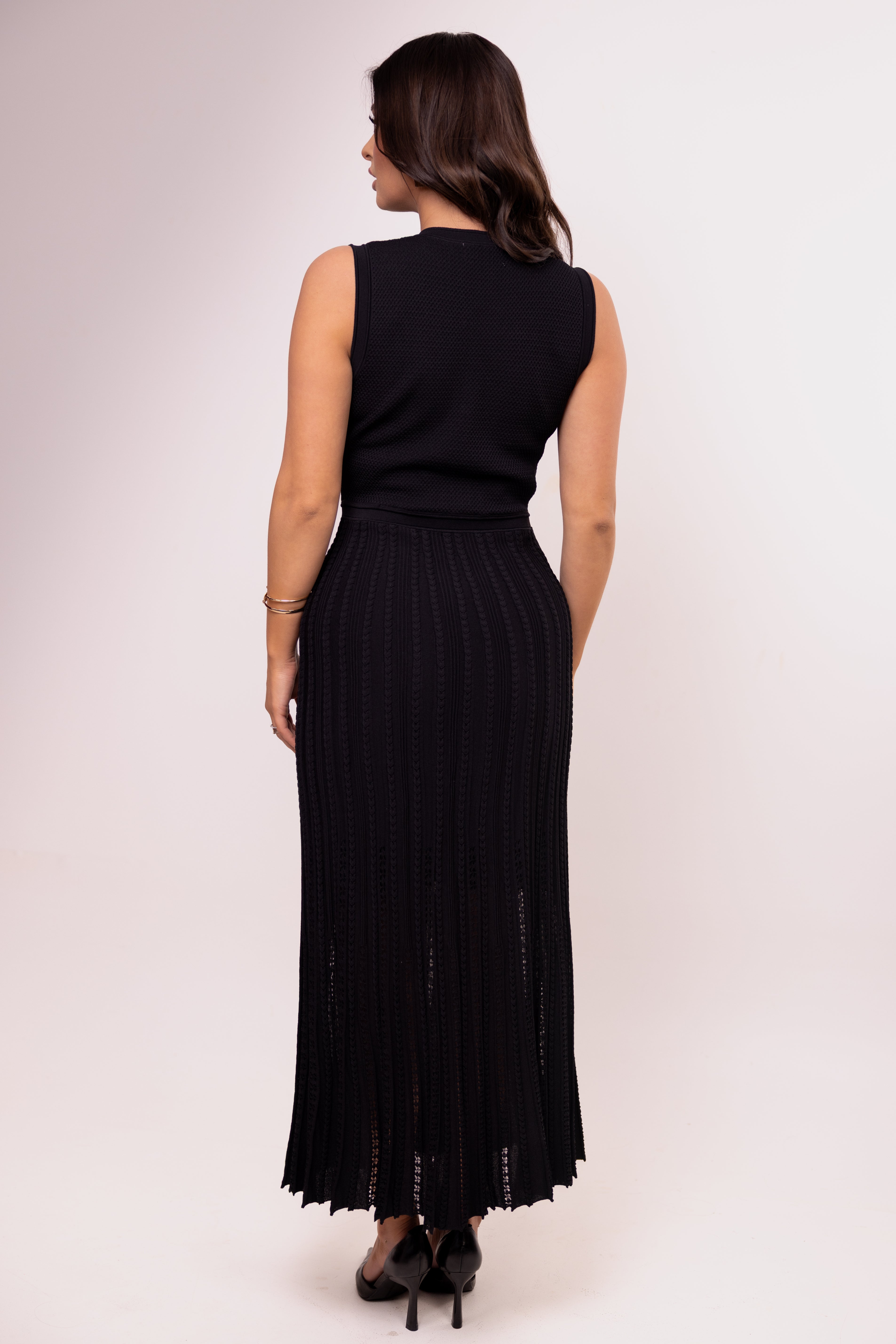 Woman wearing a black sleeveless top and black pleated skirt on a white background