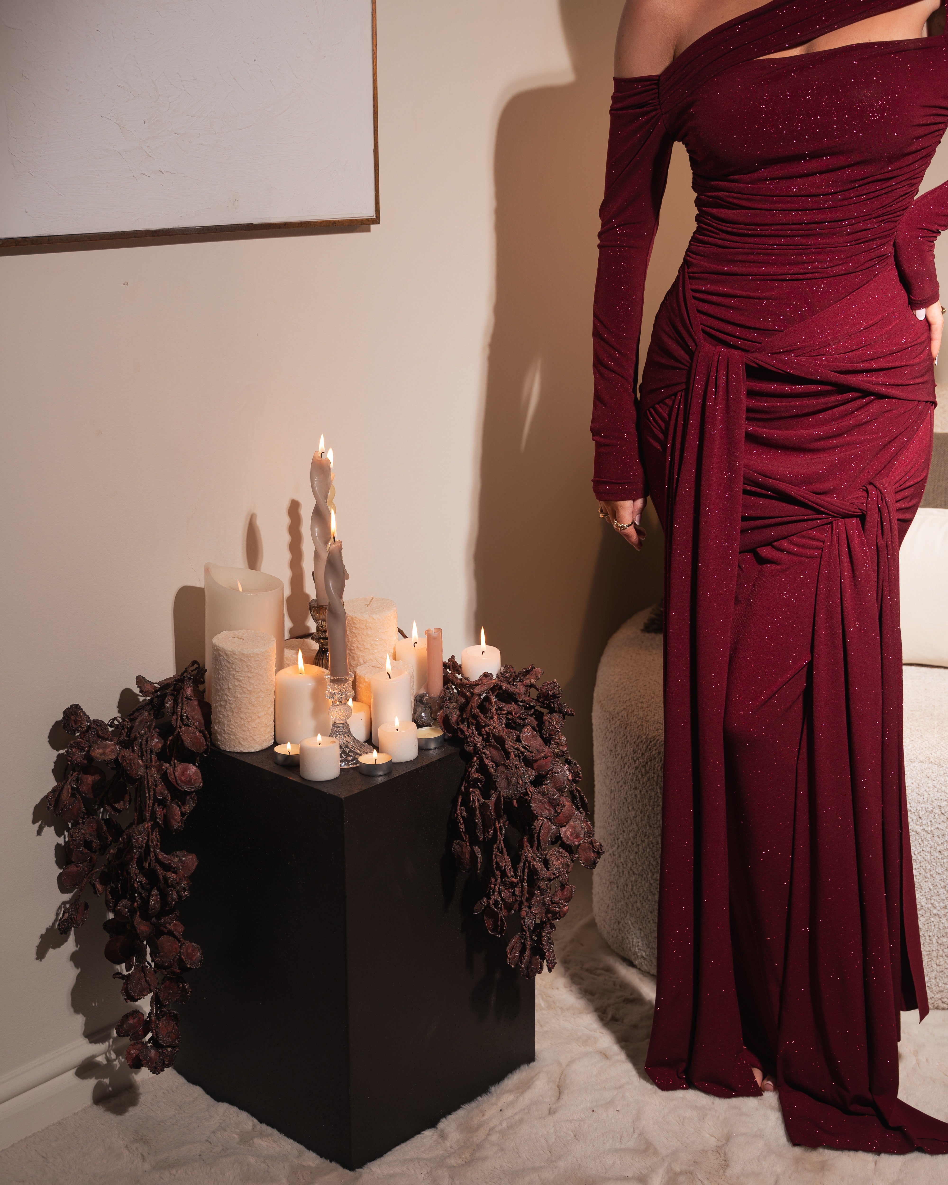 Woman in a burgundy evening gown standing next to a table with candles and decorative elements.
