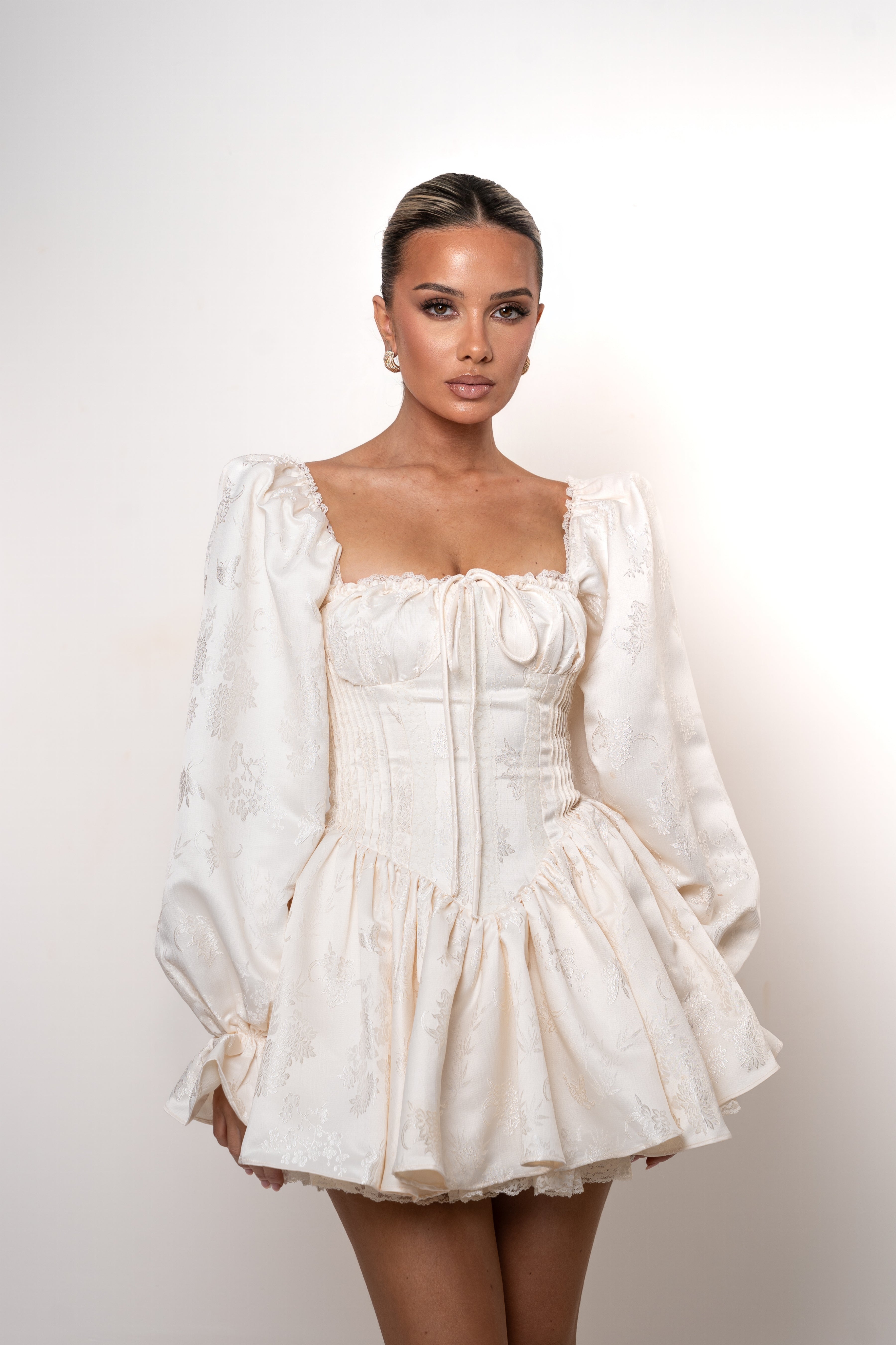 Woman wearing a white dress with long sleeves against a plain background