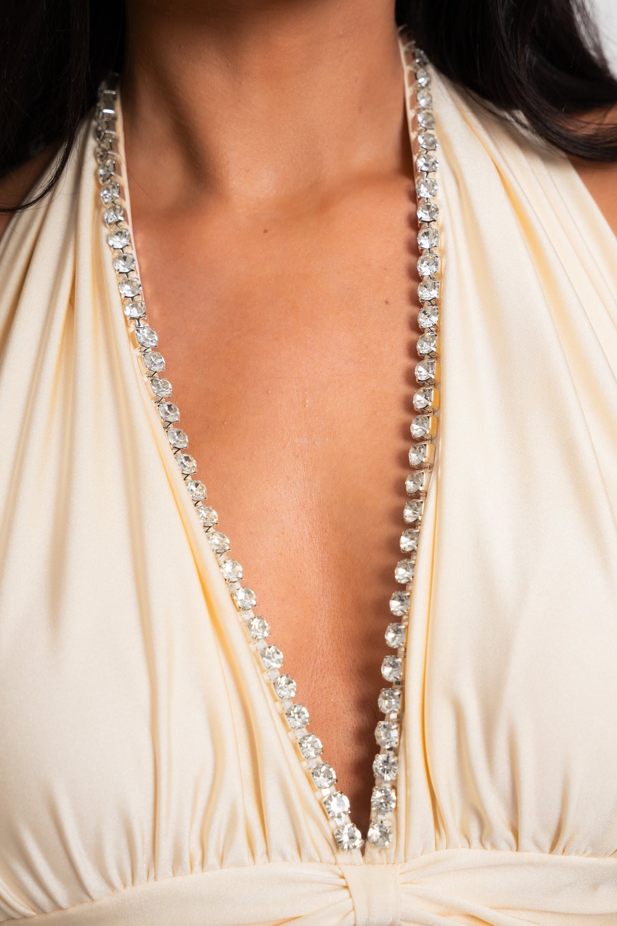Close-up of a cream-colored halter dress with a deep V-neckline, heavily embellished with sparkling clear rhinestones along the edges of the neckline.
