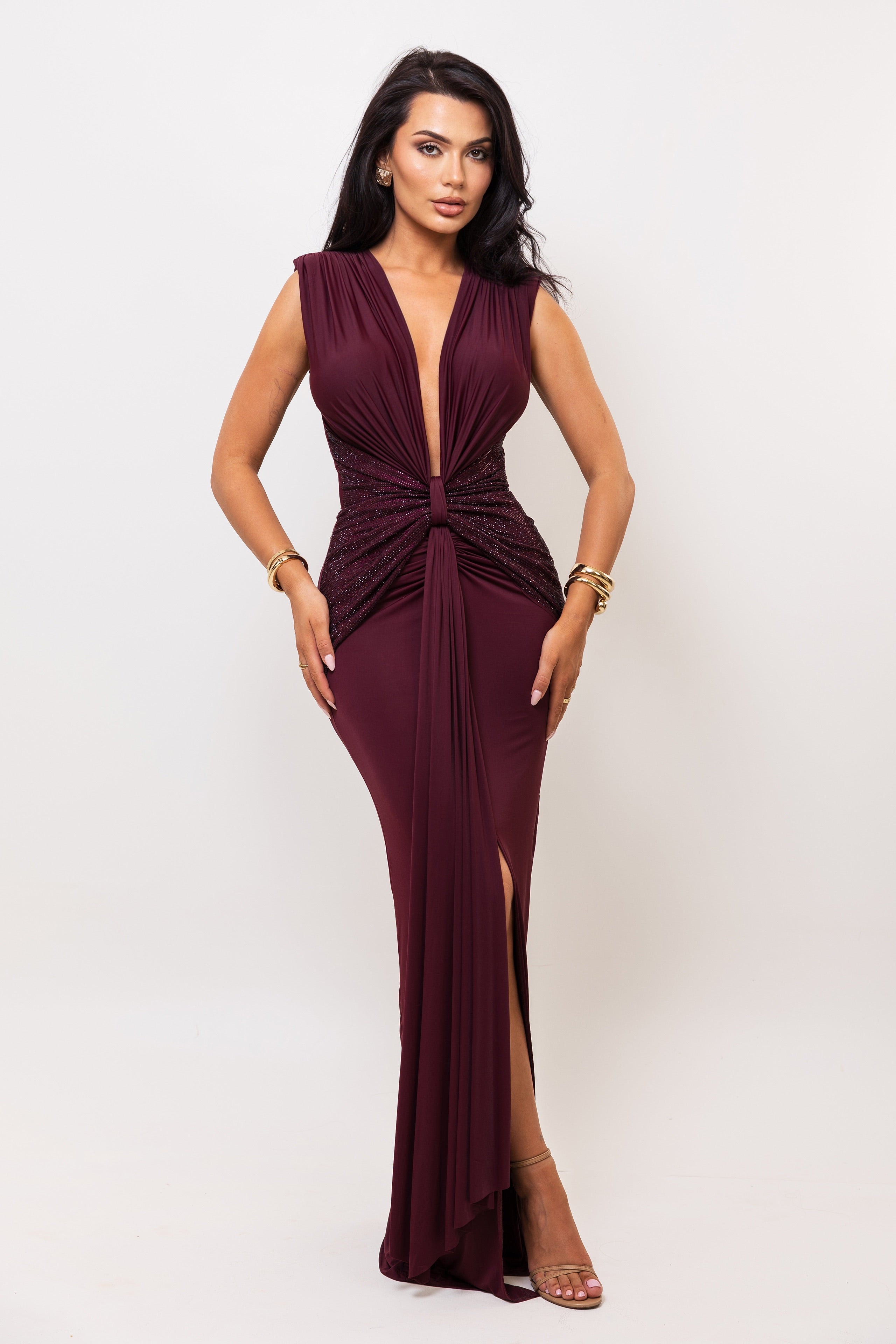 Woman wearing a burgundy evening gown with a plunging neckline and slit on a white background