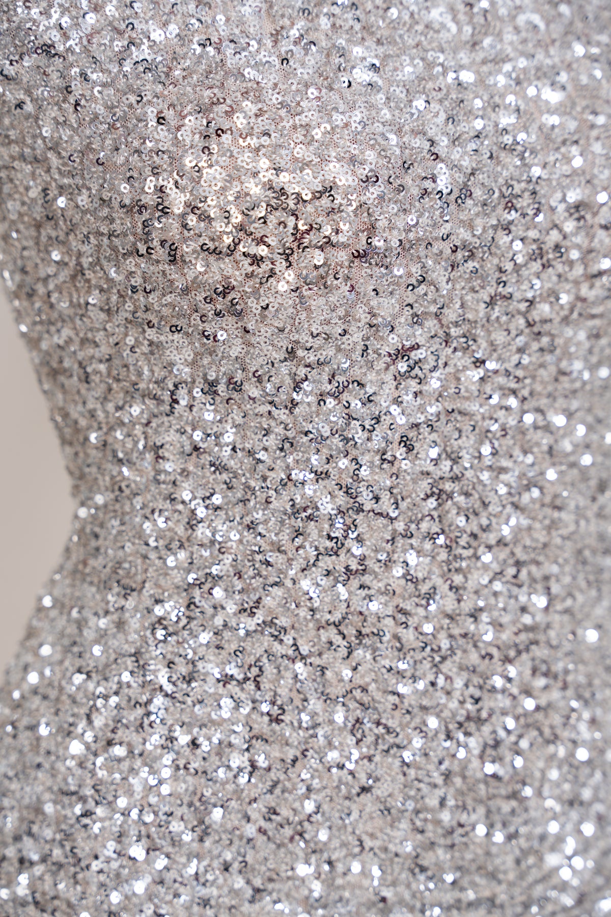 Close-up of a silver sequined fabric with dense reflective glitter texture on a mannequin or dress form.