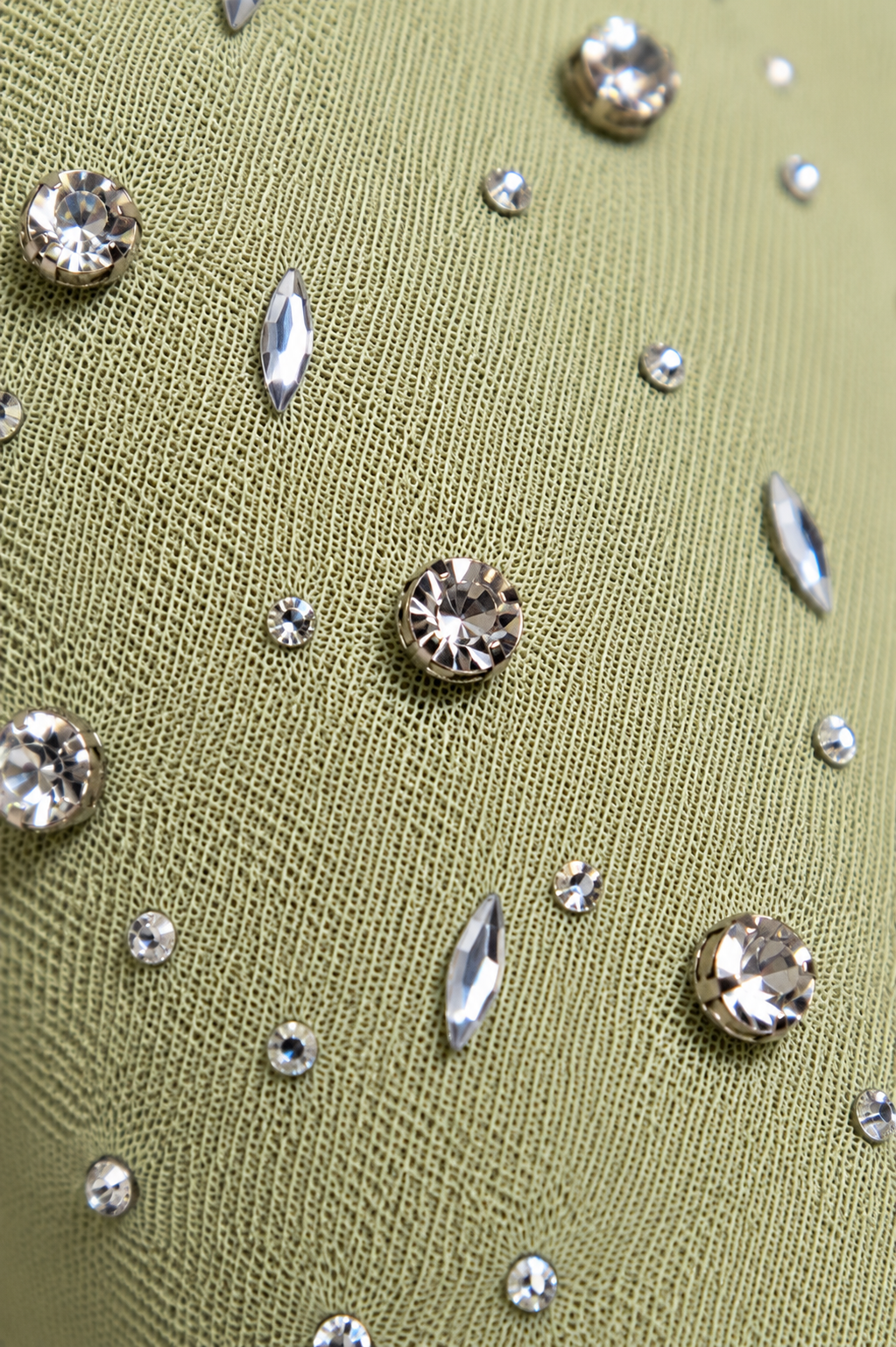 Close-up of olive green textured fabric adorned with scattered clear rhinestones and faceted crystal embellishments in round and marquise settings.