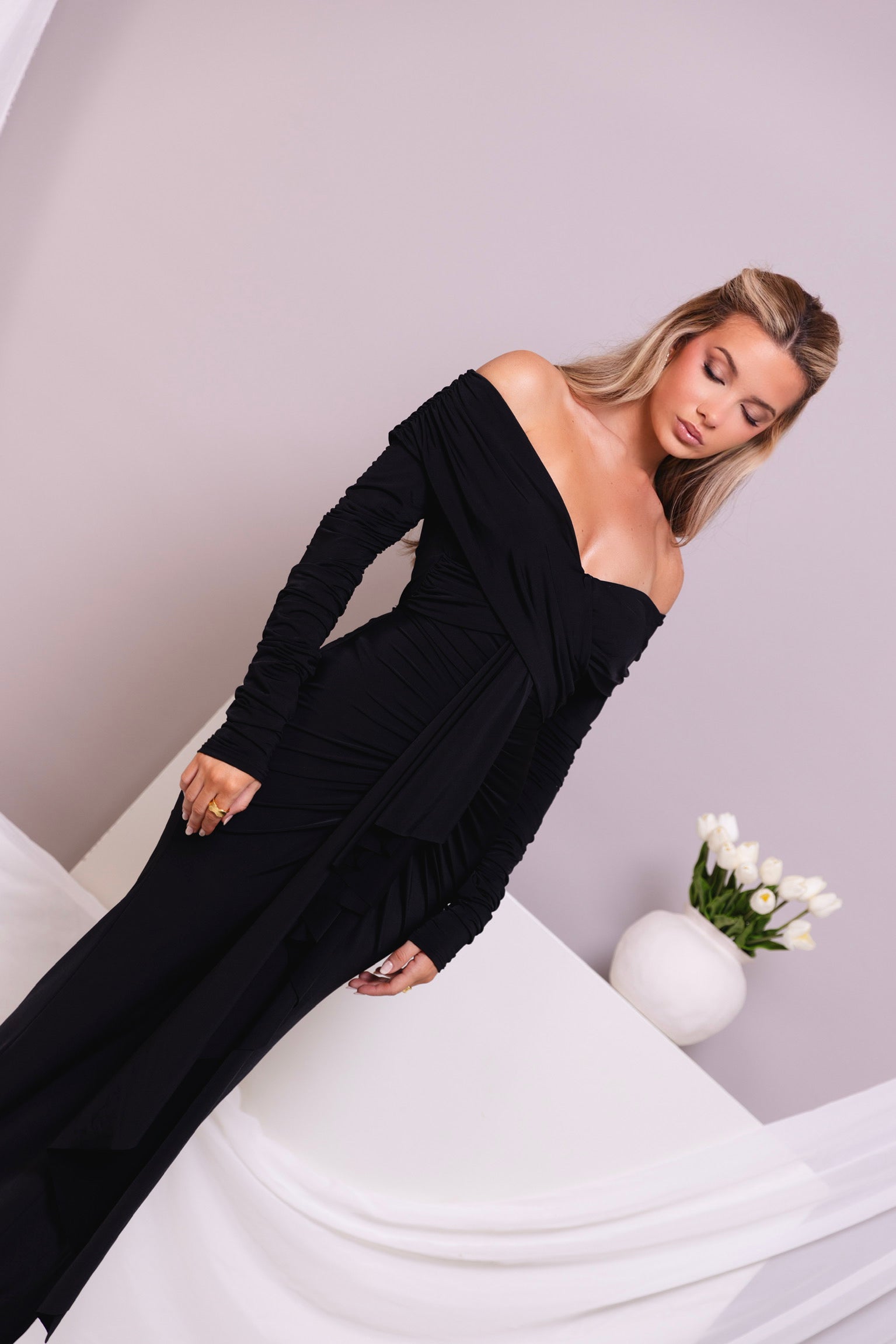 Figure-hugging black evening gown with a bold off-the-shoulder cut and draped finish.