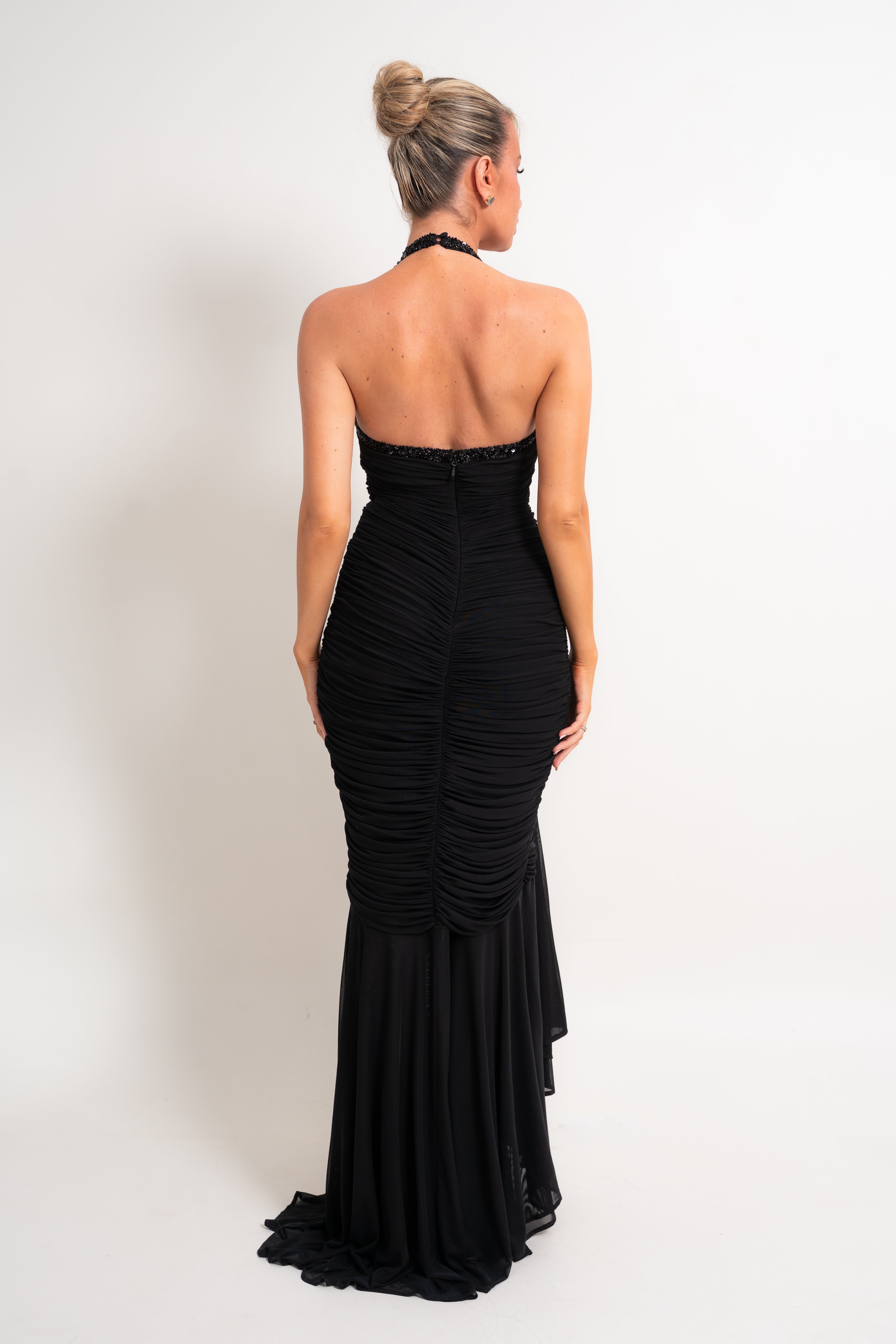 A woman wearing a black strapless ruched mermaid gown, shown from the back against a plain white studio background.