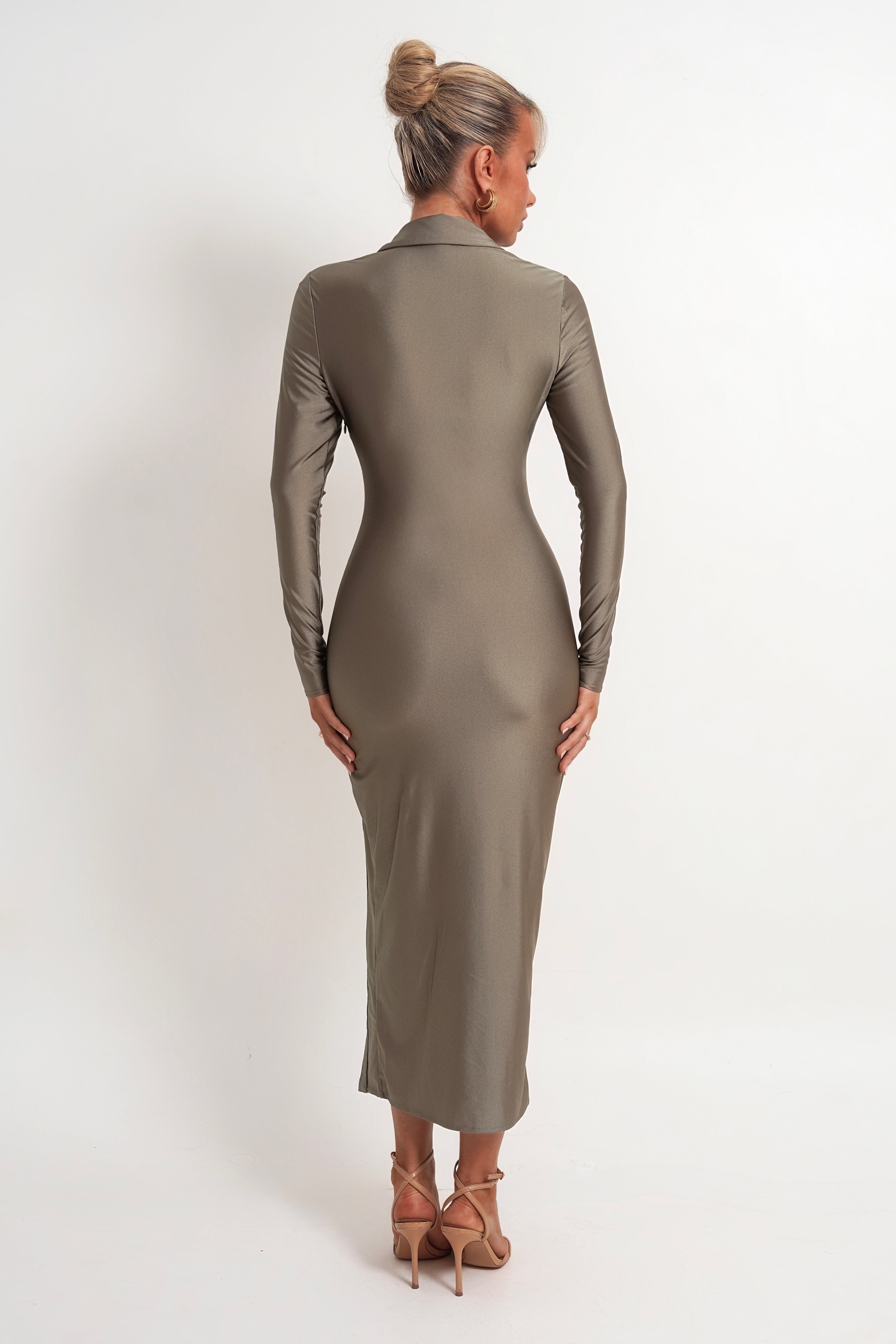 A woman viewed from the back wearing a fitted long-sleeve midi dress in a taupe-brown color, paired with tan high-heeled sandals, against a plain white studio background.