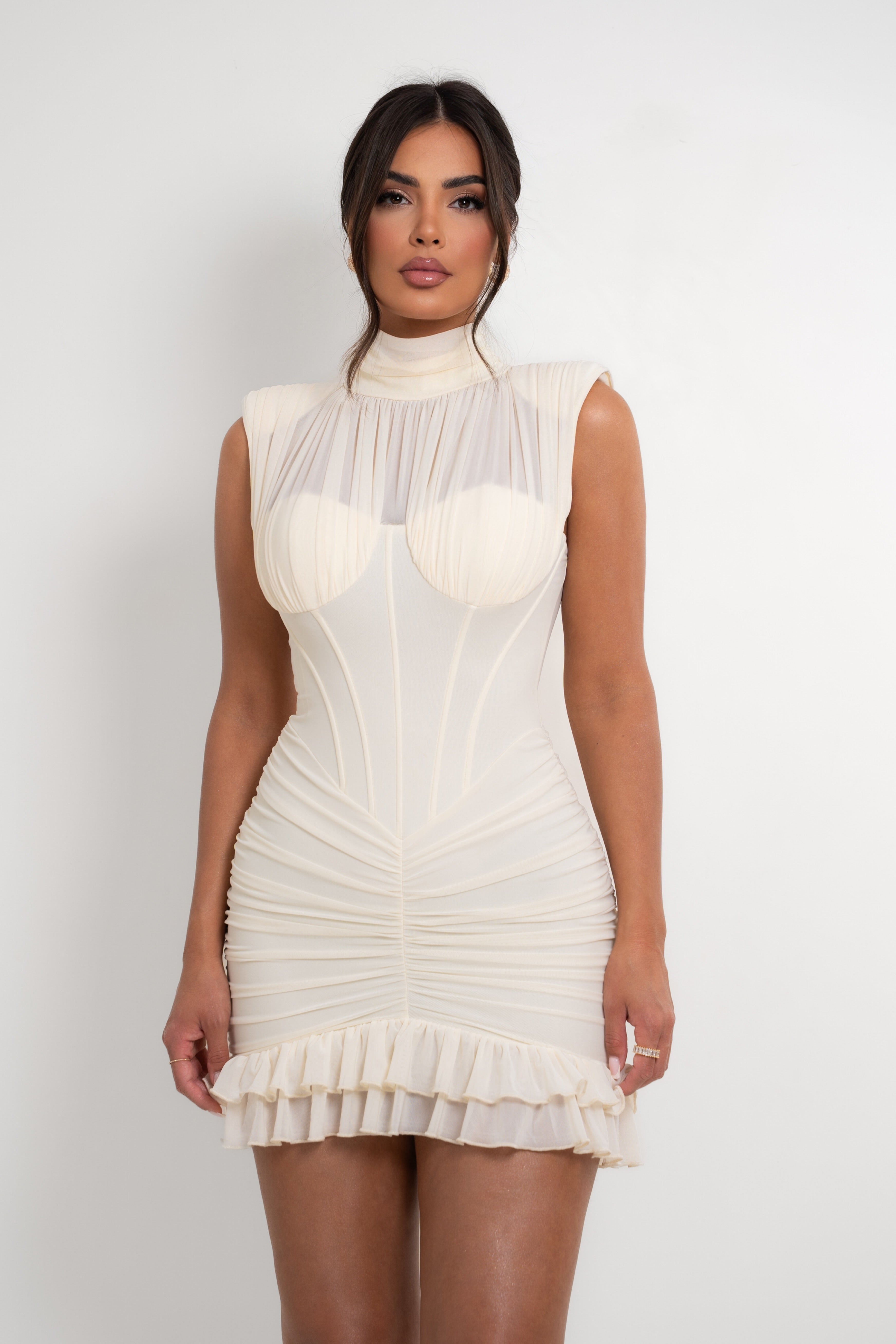 Woman wearing a white dress with a sheer overlay on a plain background