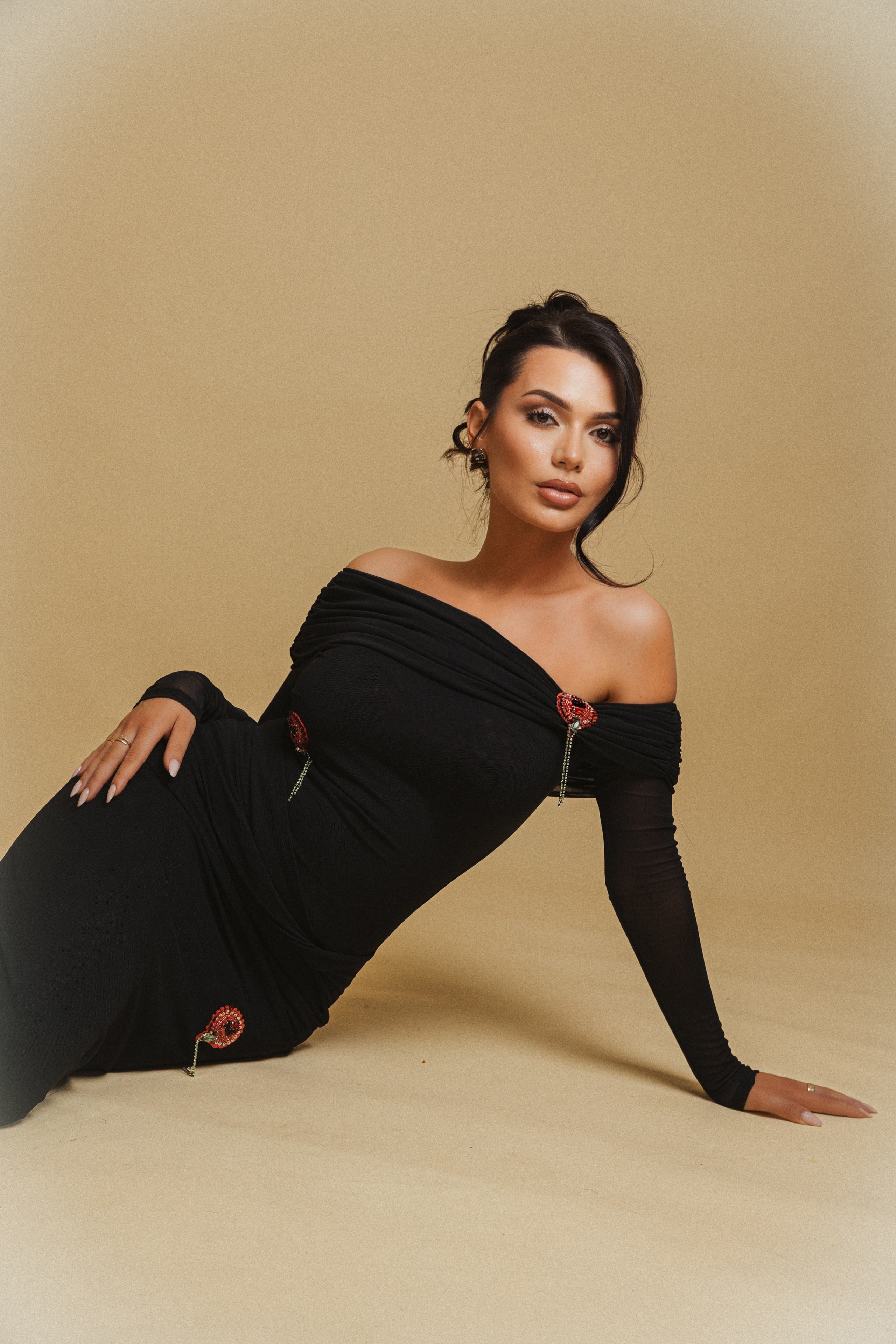 Woman in a black off-shoulder dress posing on a beige background
