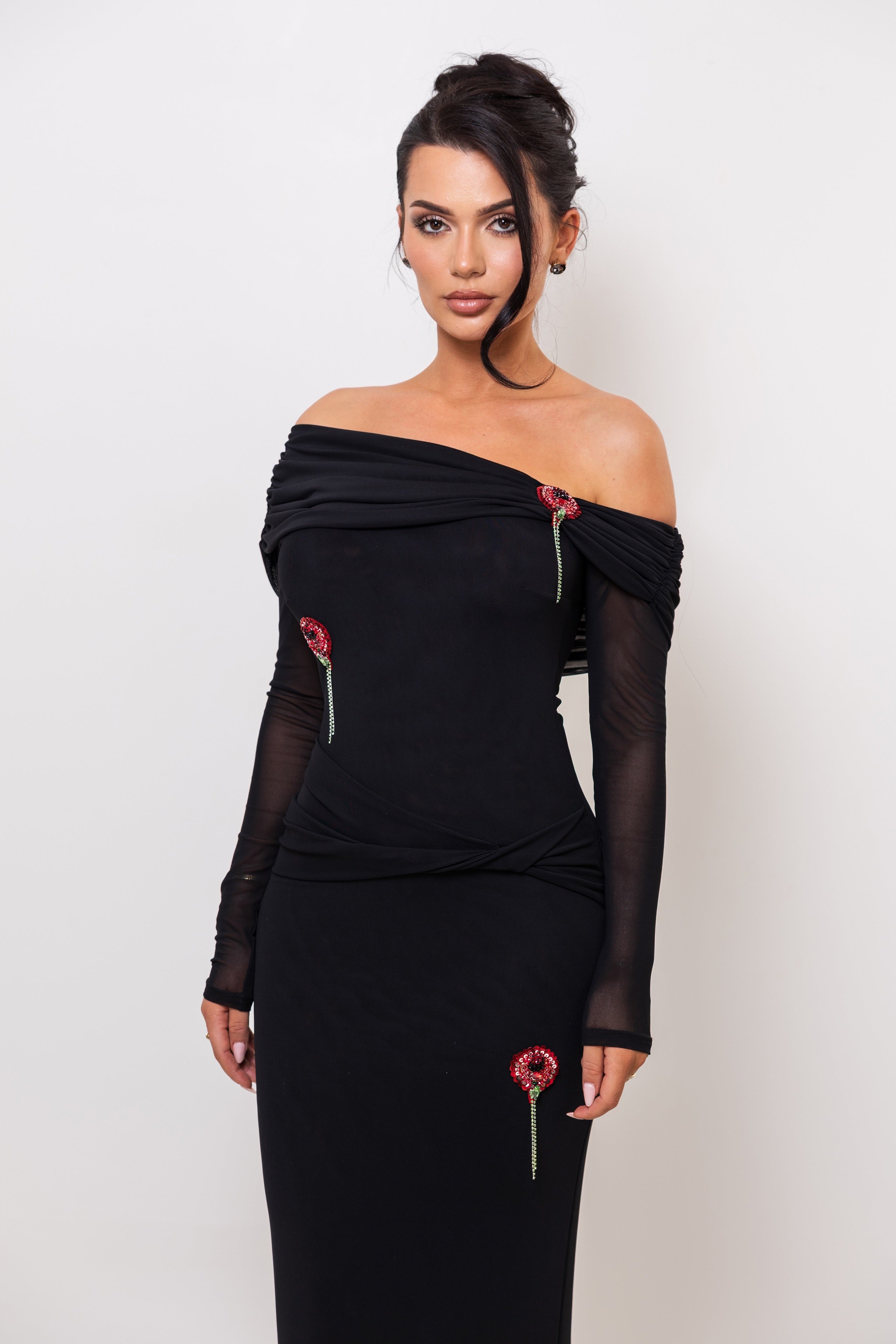 Woman wearing a black off-shoulder dress with sheer sleeves against a white background