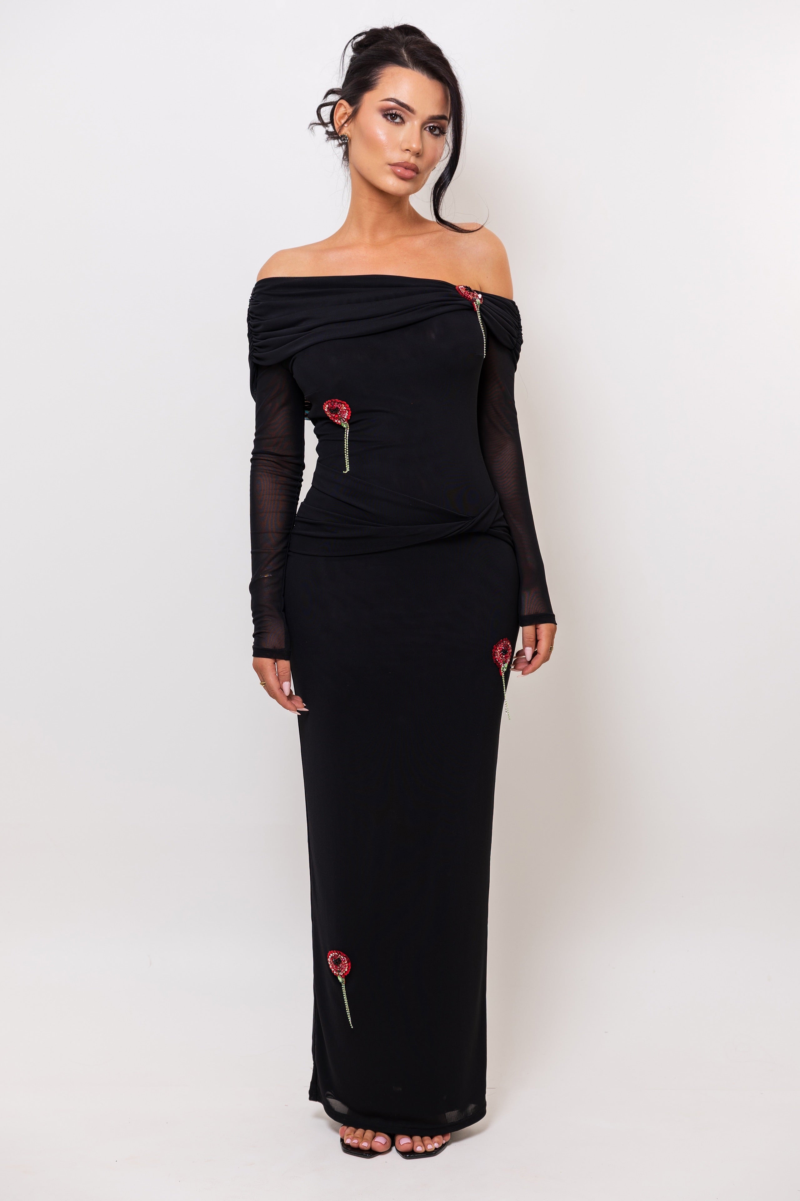 Woman wearing a black off-shoulder dress with floral details on a white background