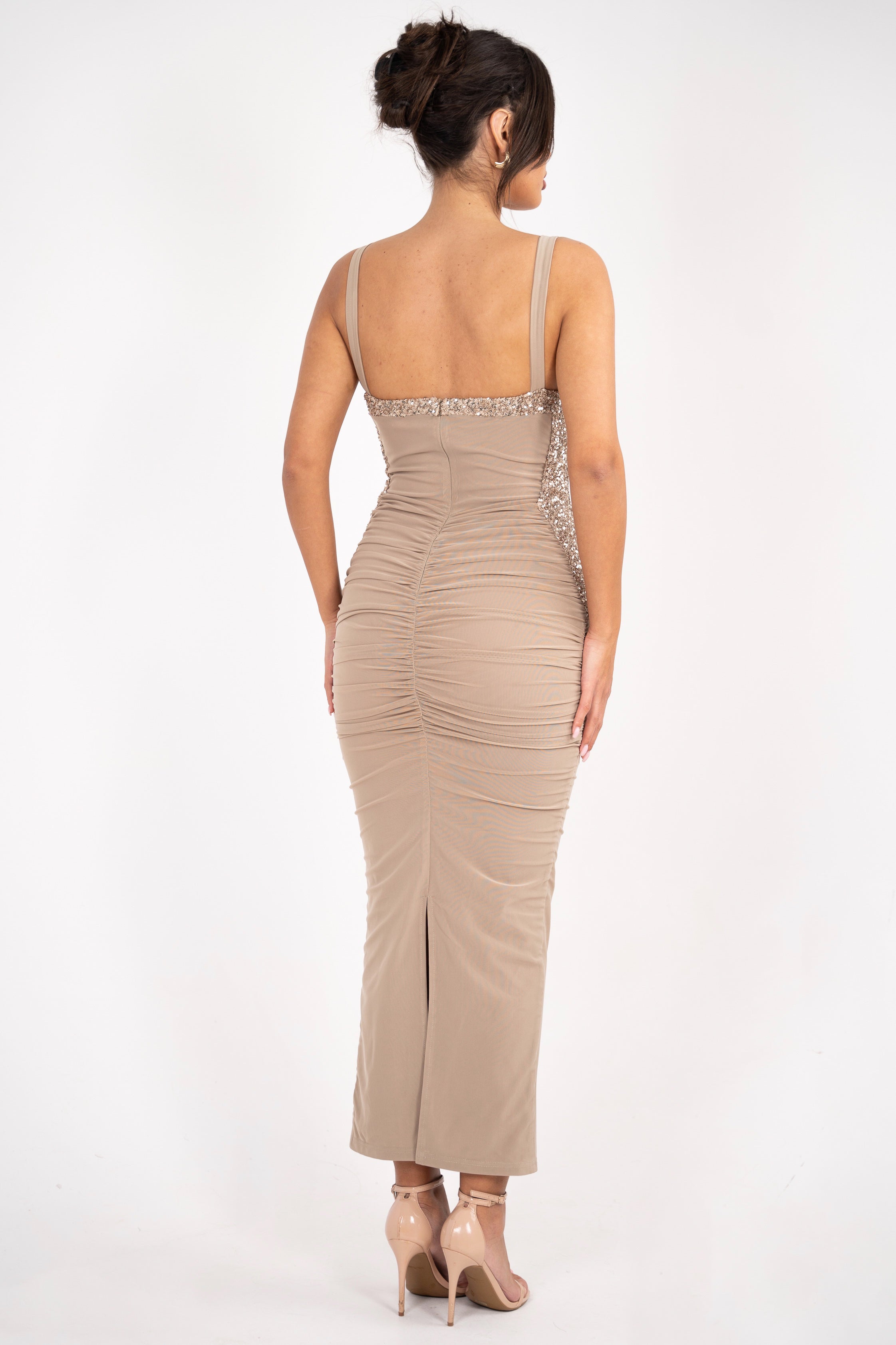 A glamorous, body-hugging beige dress featuring shimmering beaded detailing at the neckline, ruched design, and delicate spaghetti straps.