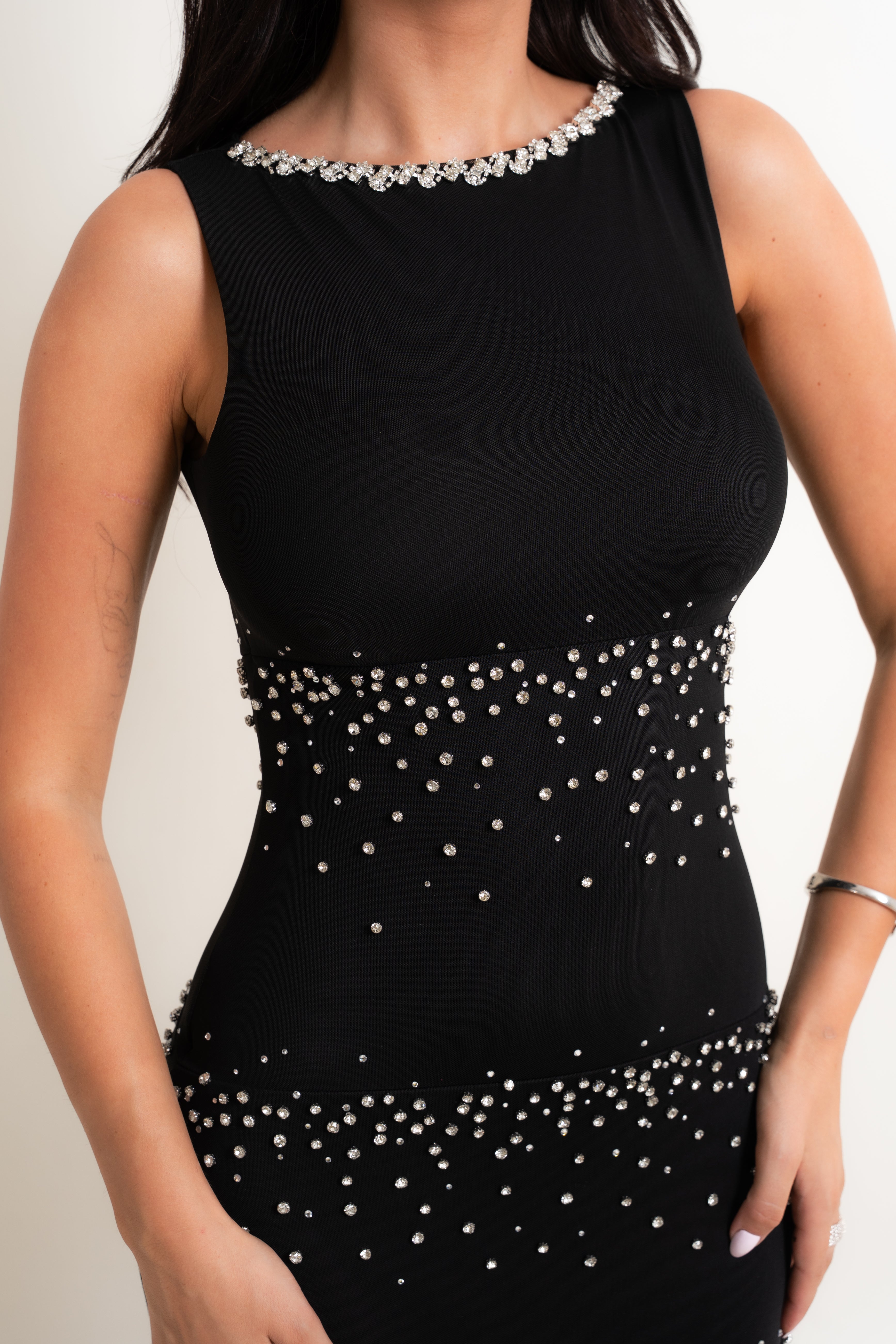 A sleeveless black ribbed dress with silver rhinestone embellishments around the scoop neckline, waist, and hem, shown on a model against a light background.