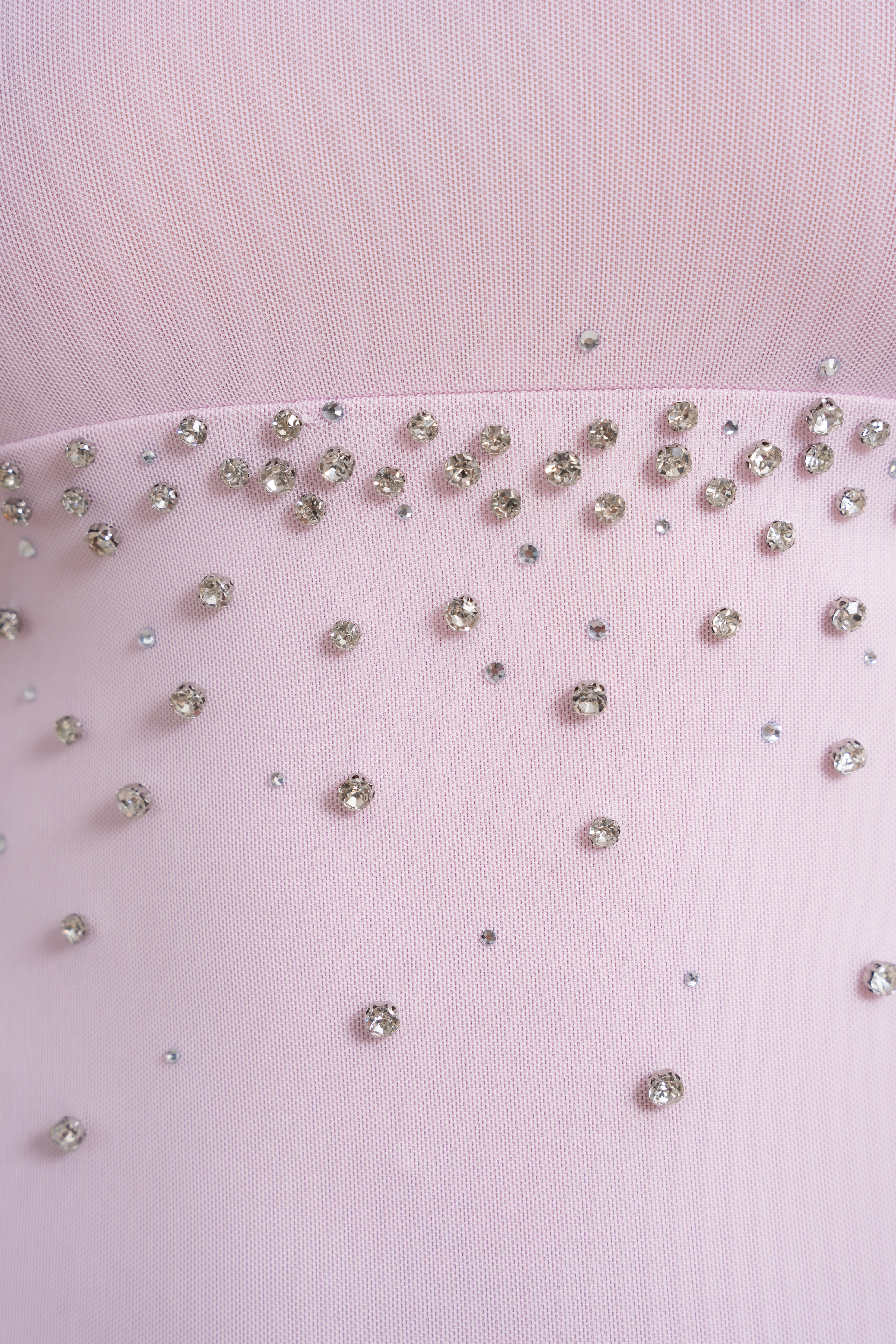 Close-up of a light pink fabric surface with scattered clear rhinestones and small metallic embellishments.