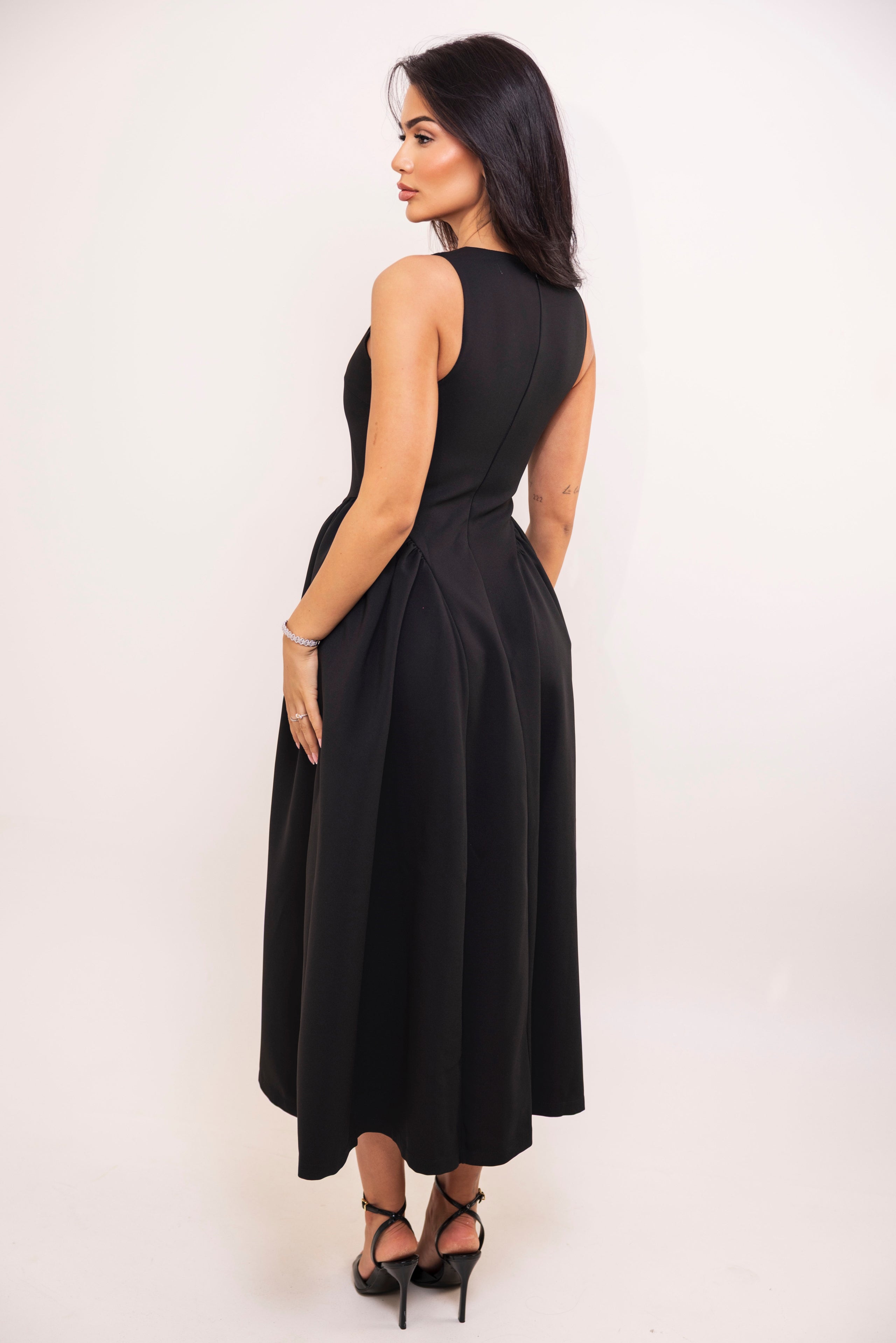 Back view of sleeveless black dress with full pleated skirt.