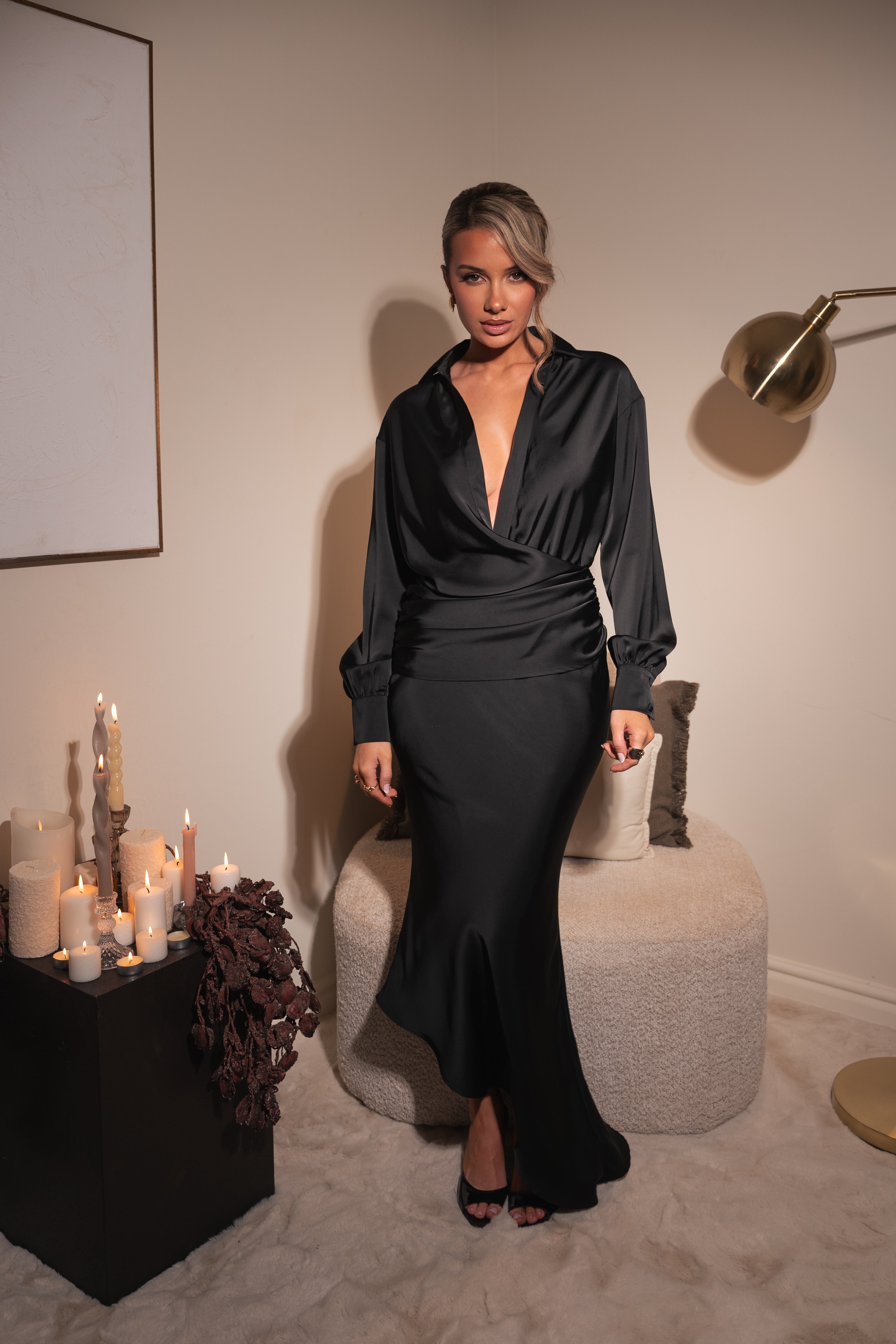 Woman in a black satin dress standing in a room with candles and decor.
