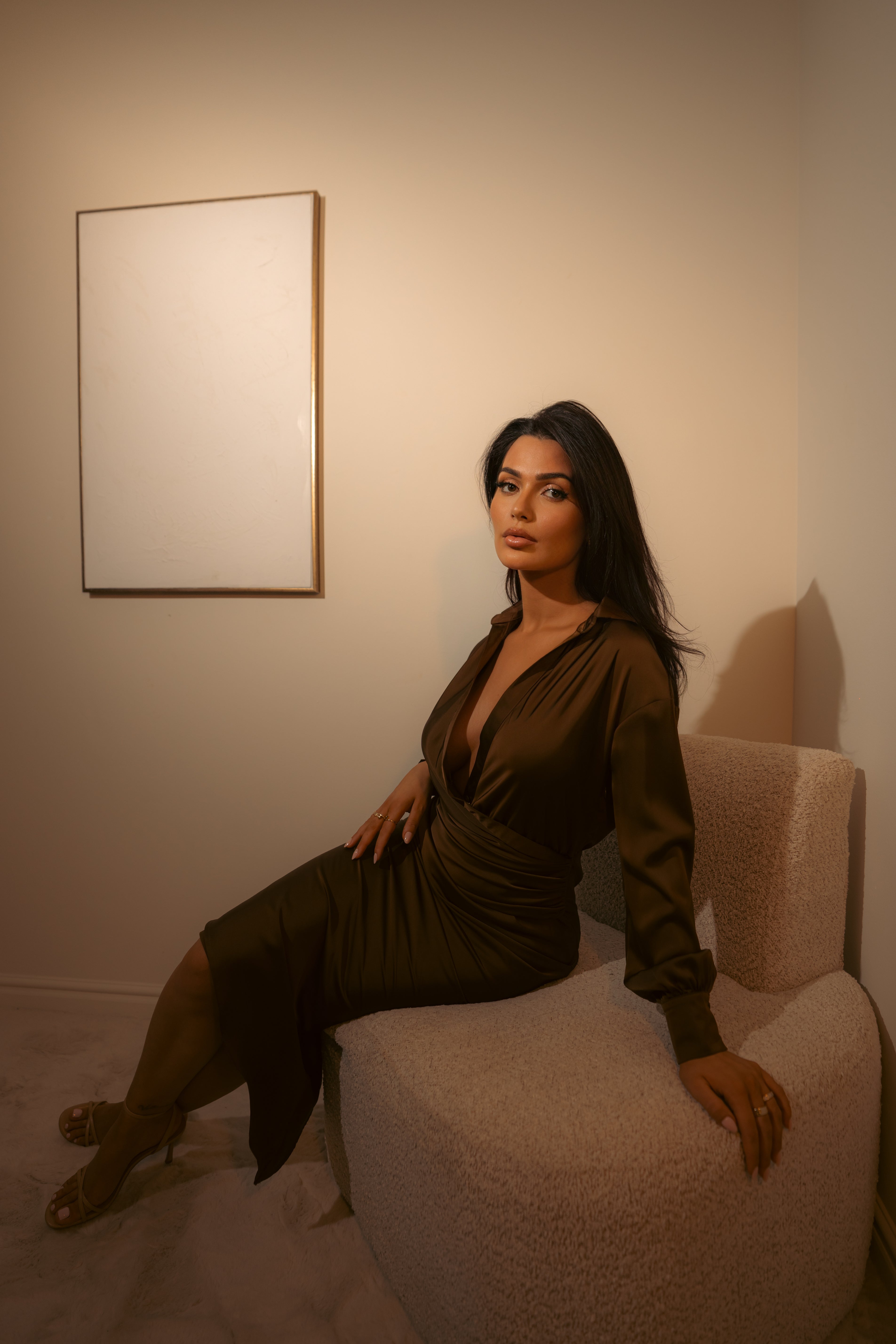 Woman in a green dress sitting on a chair in a room with a plain wall and a framed picture.
