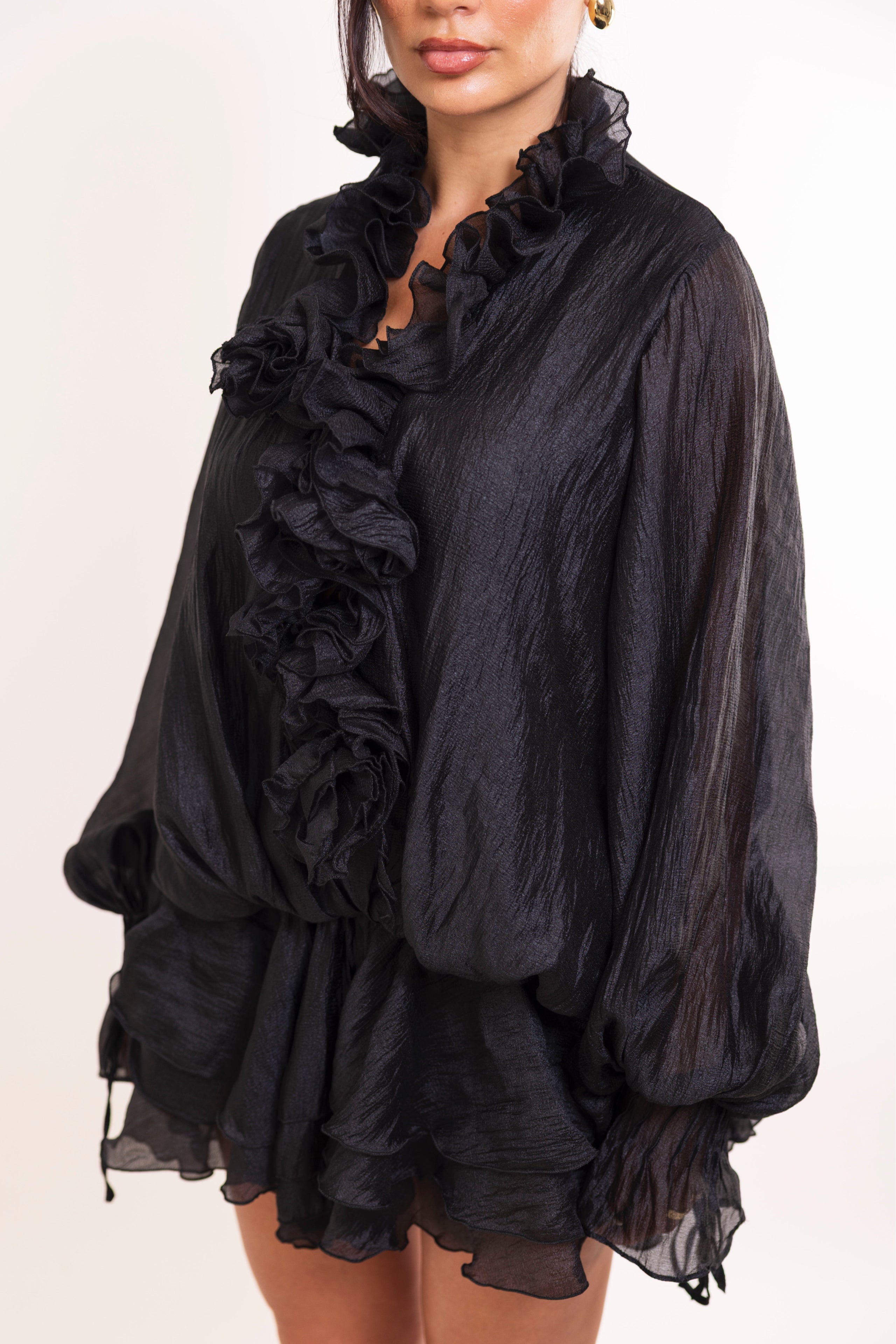 Front view of sheer textured black dress styled with gold earrings and heels.