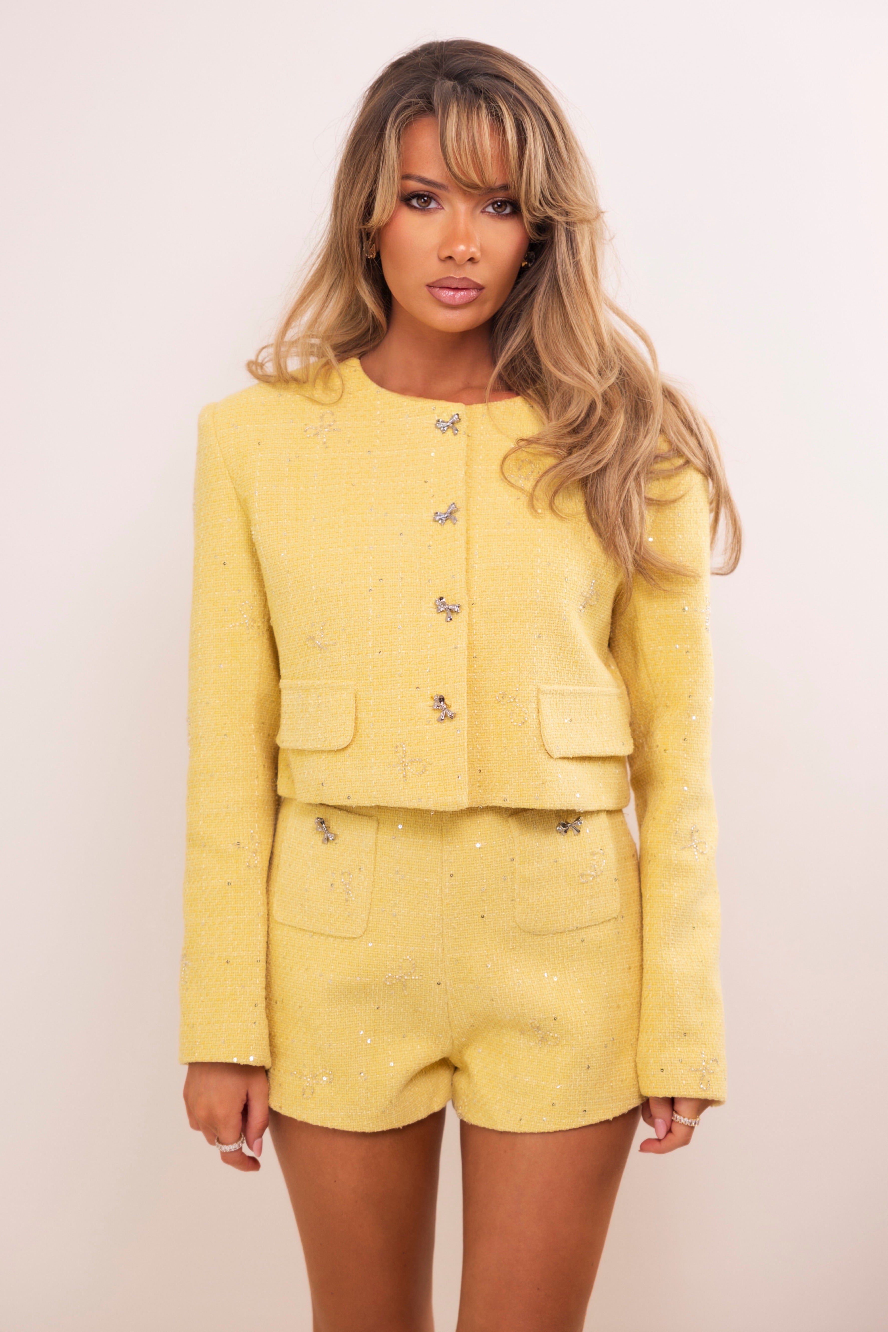 Close-up of embellished yellow tweed jacket with flap pockets and rhinestone bow closures