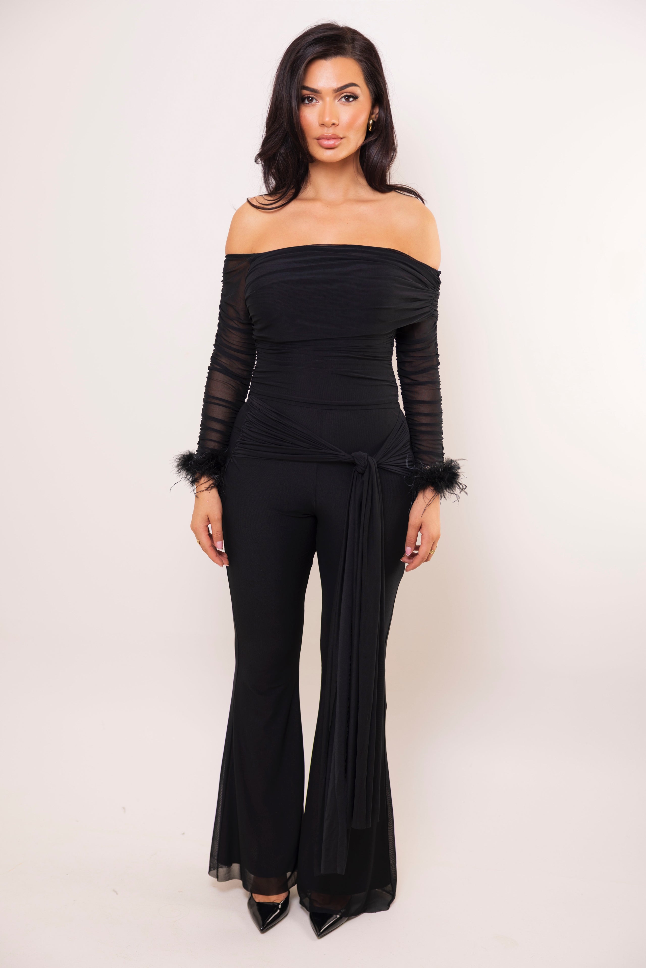Rear view of black ruched off-shoulder jumpsuit with fitted silhouette and flared legs.