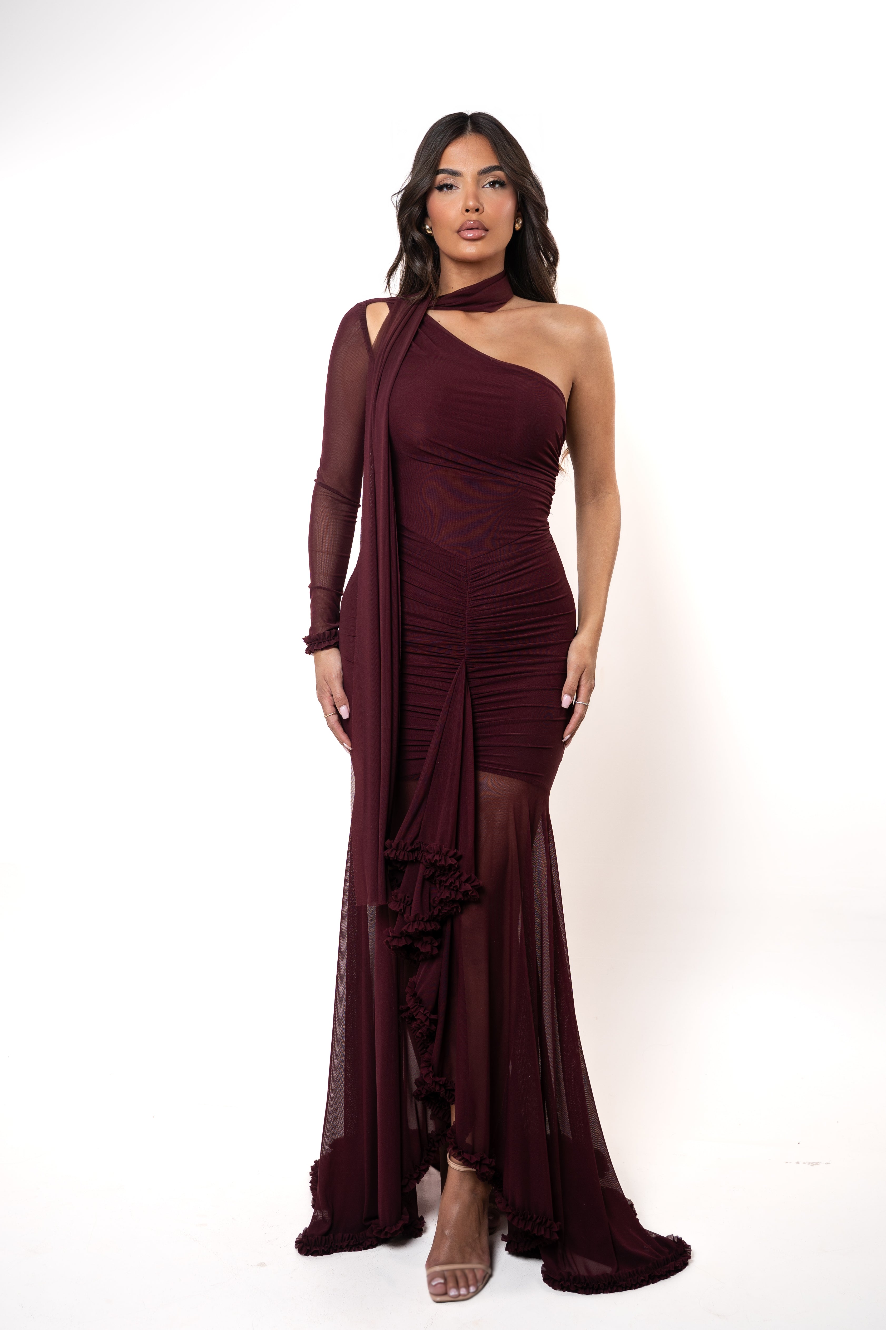 Woman wearing a burgundy one-shoulder dress with a sheer overlay on a white background