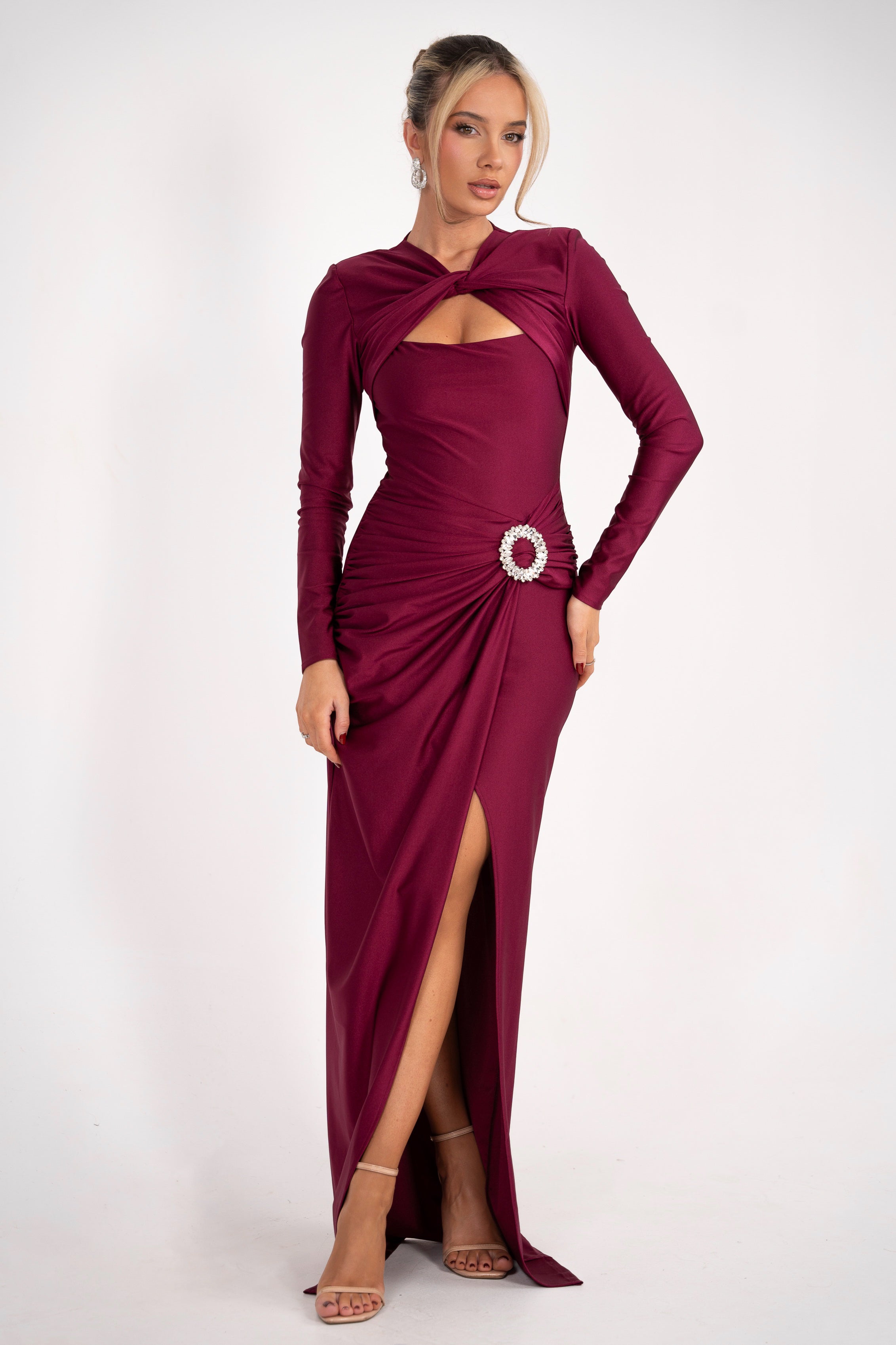 A floor-length plum dress with intricate pleating, a fitted bodice, and a statement crystal pin