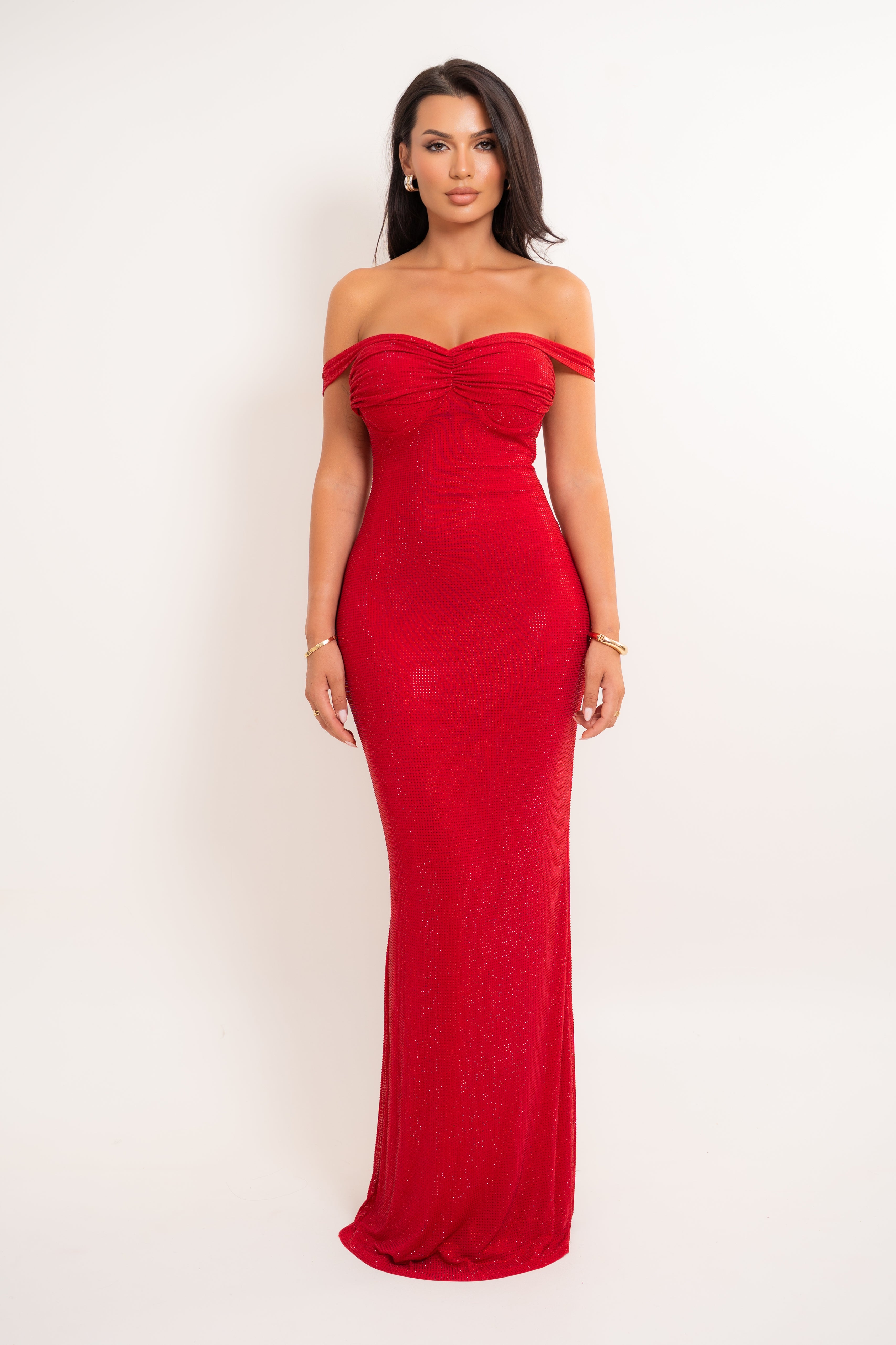 A woman modeling a red off-the-shoulder floor-length gown with a ruched bodice and fitted silhouette, photographed against a plain light background.