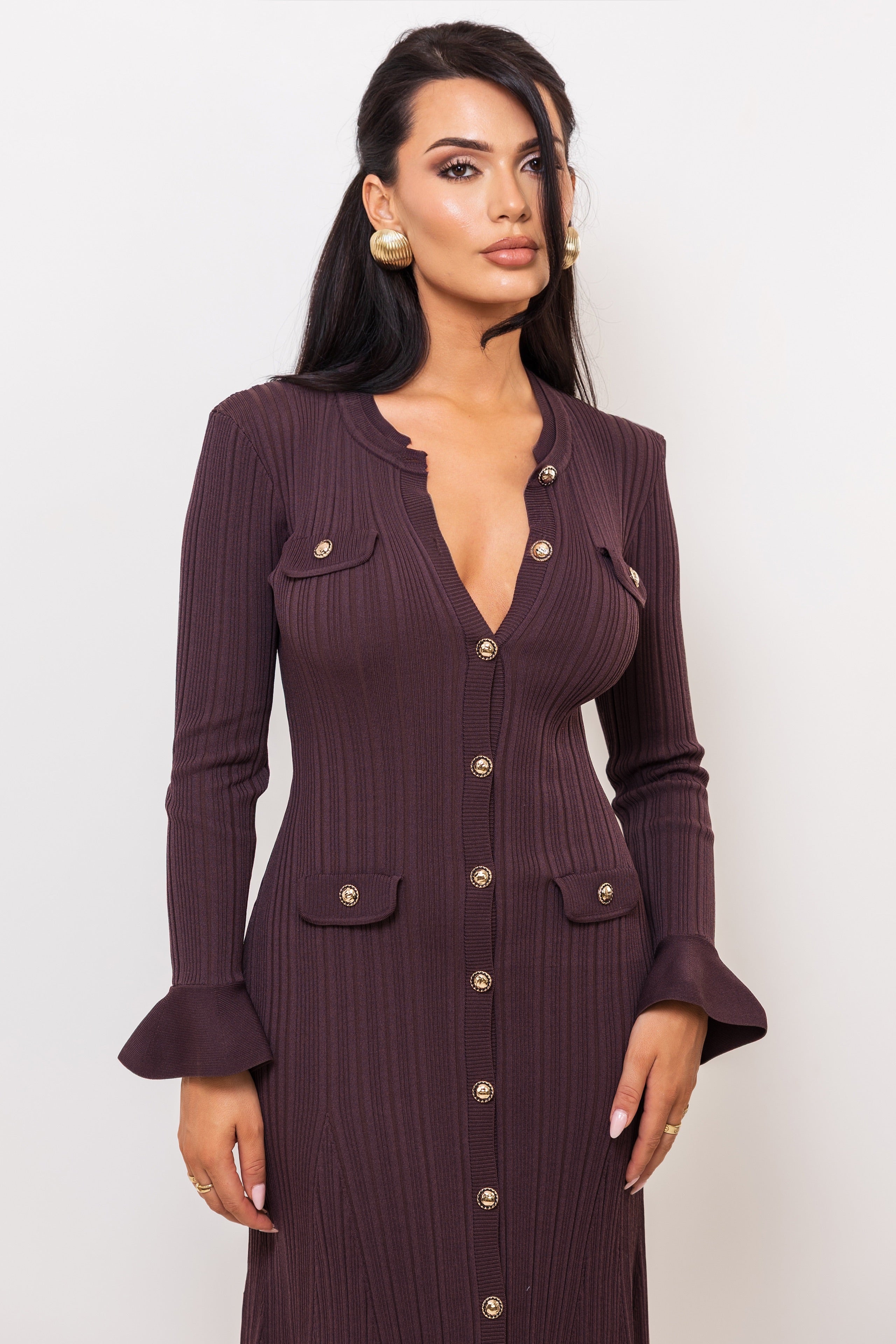 Woman wearing a deep purple ribbed dress with button details on a white background