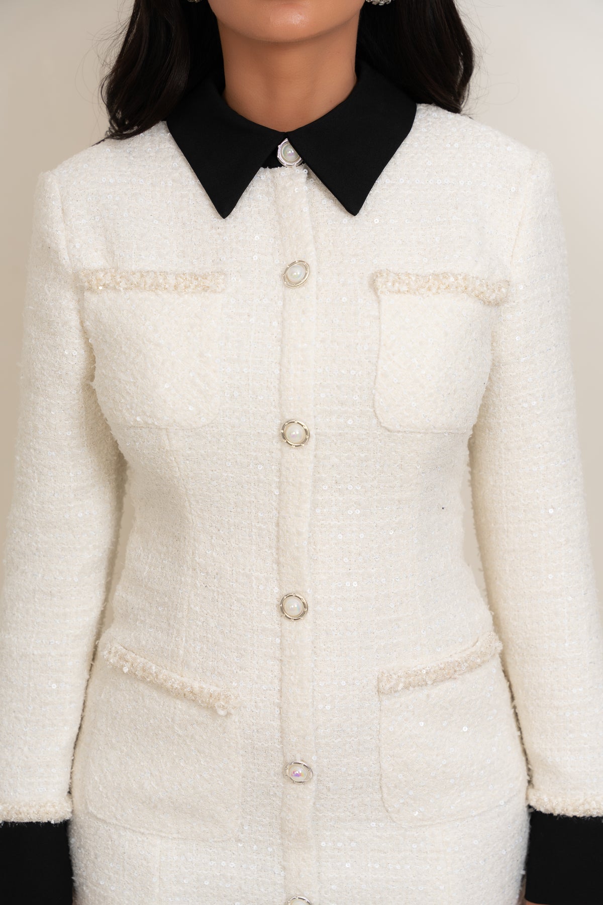A close-up of a model wearing a cream-colored tweed jacket with a black pointed collar and decorative buttons.