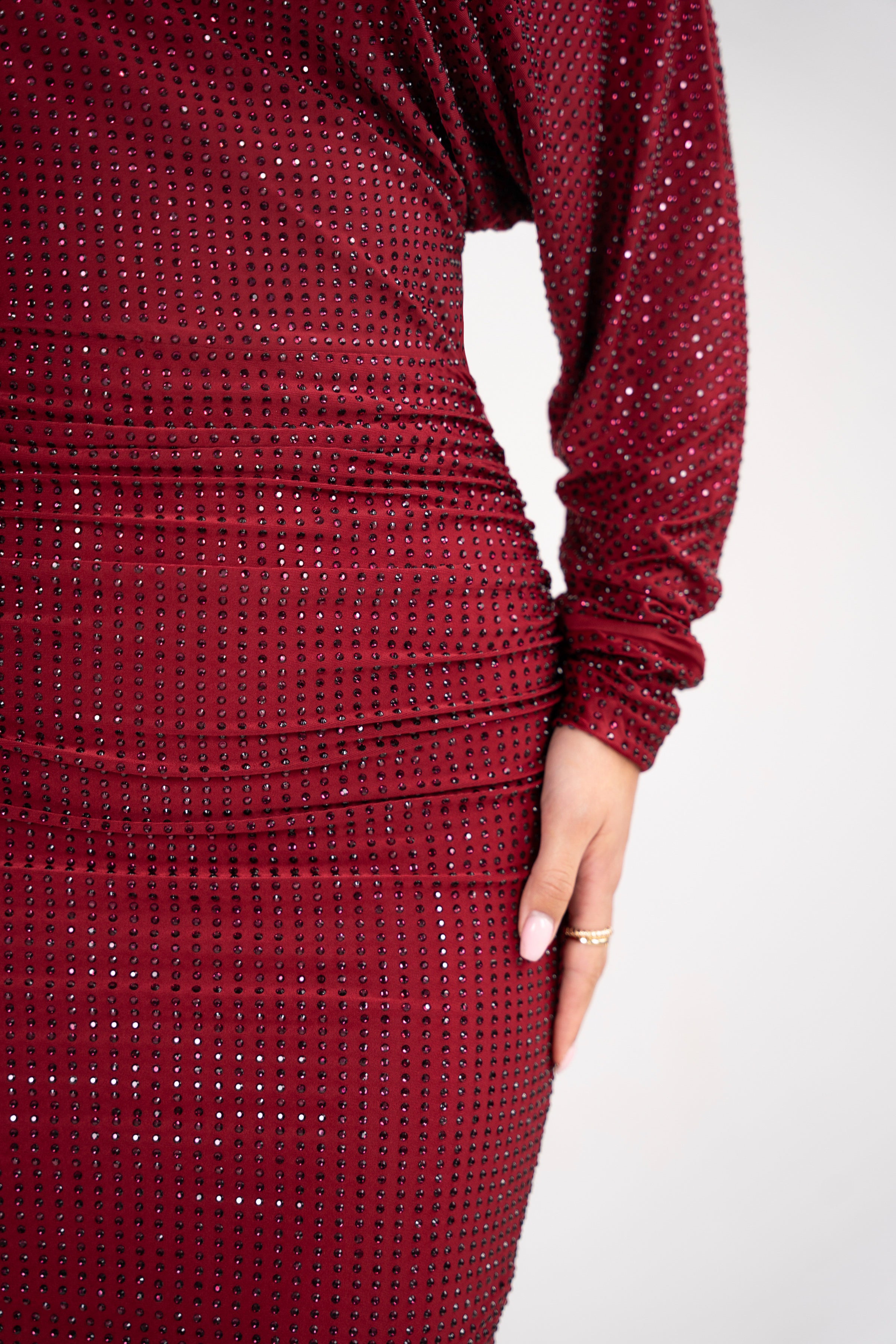 Side view of the burgundy dress showcasing the ruched detail at the hips, highlighting the figure.