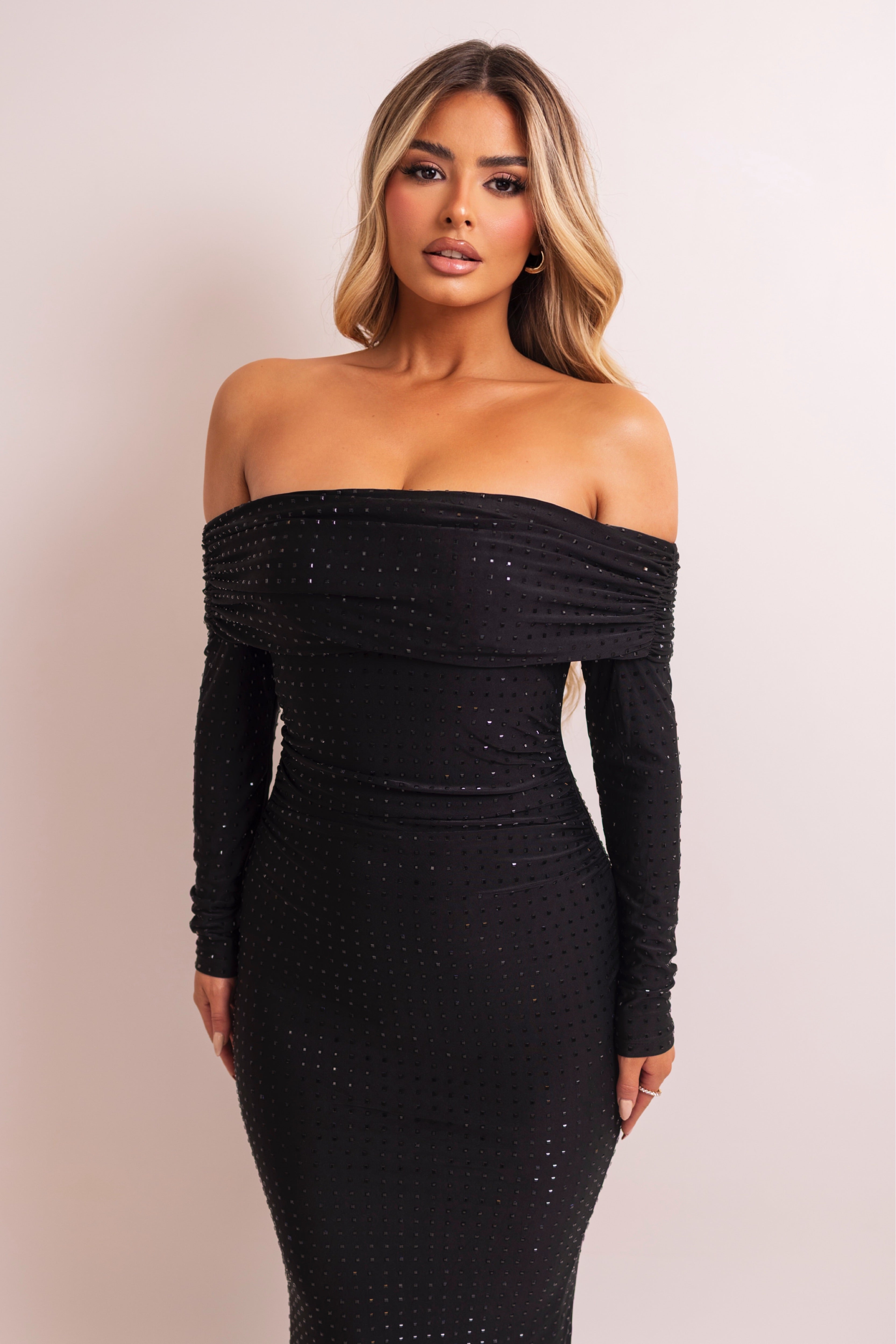 Woman wearing a black off-shoulder dress with long sleeves on a plain background