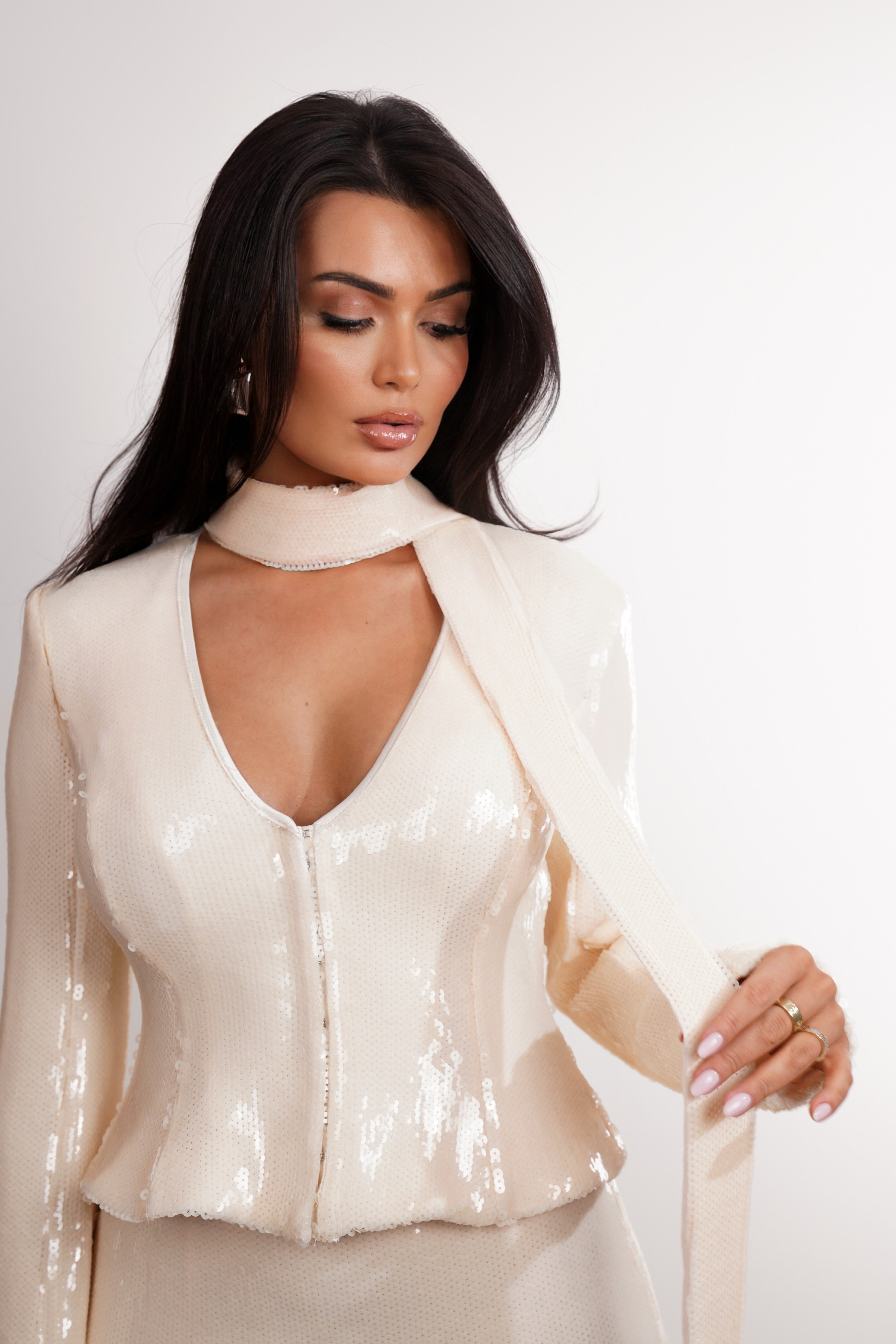Woman wearing a white sequin top against a plain background