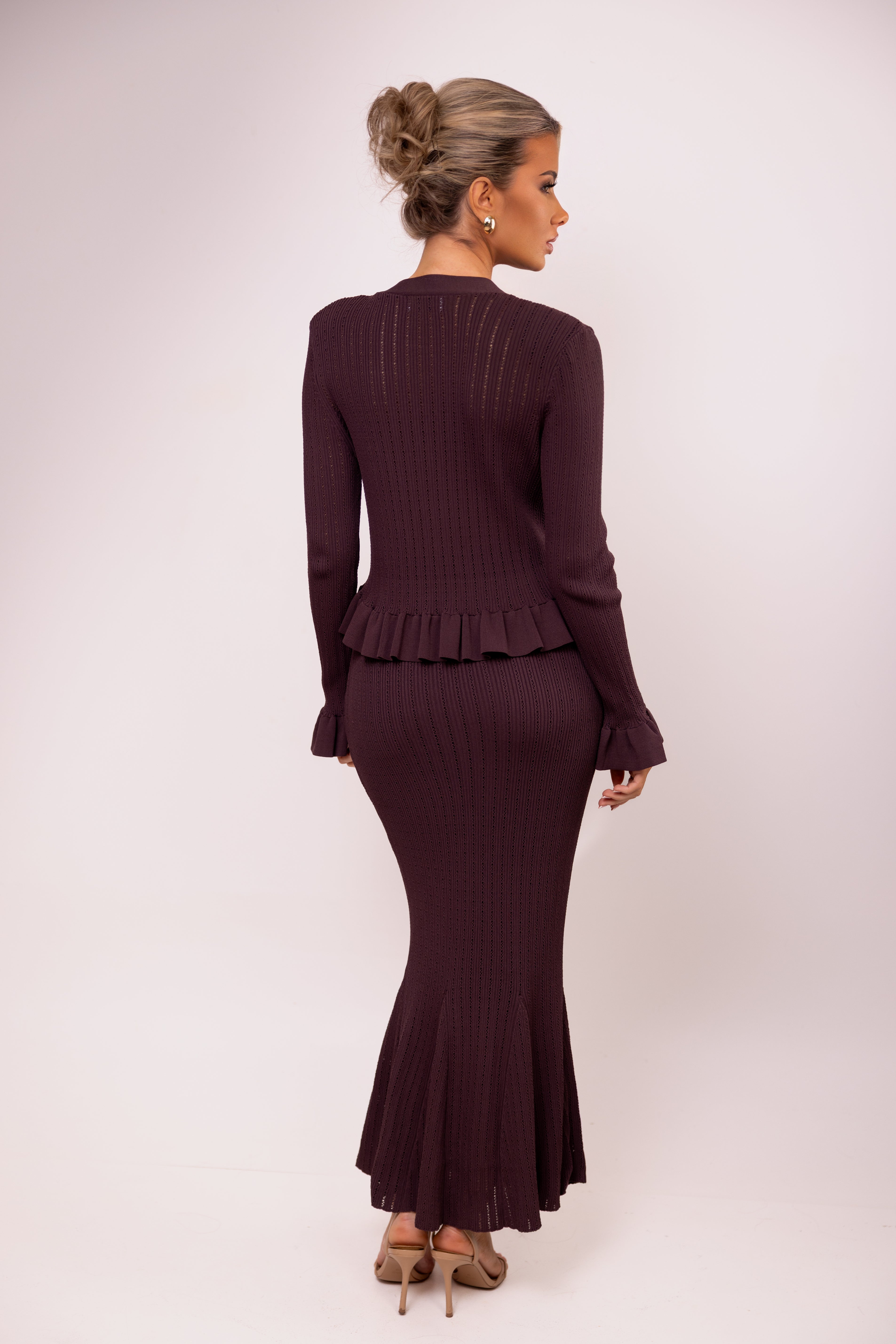 Woman wearing a dark purple ribbed dress with peplum waist on a white background