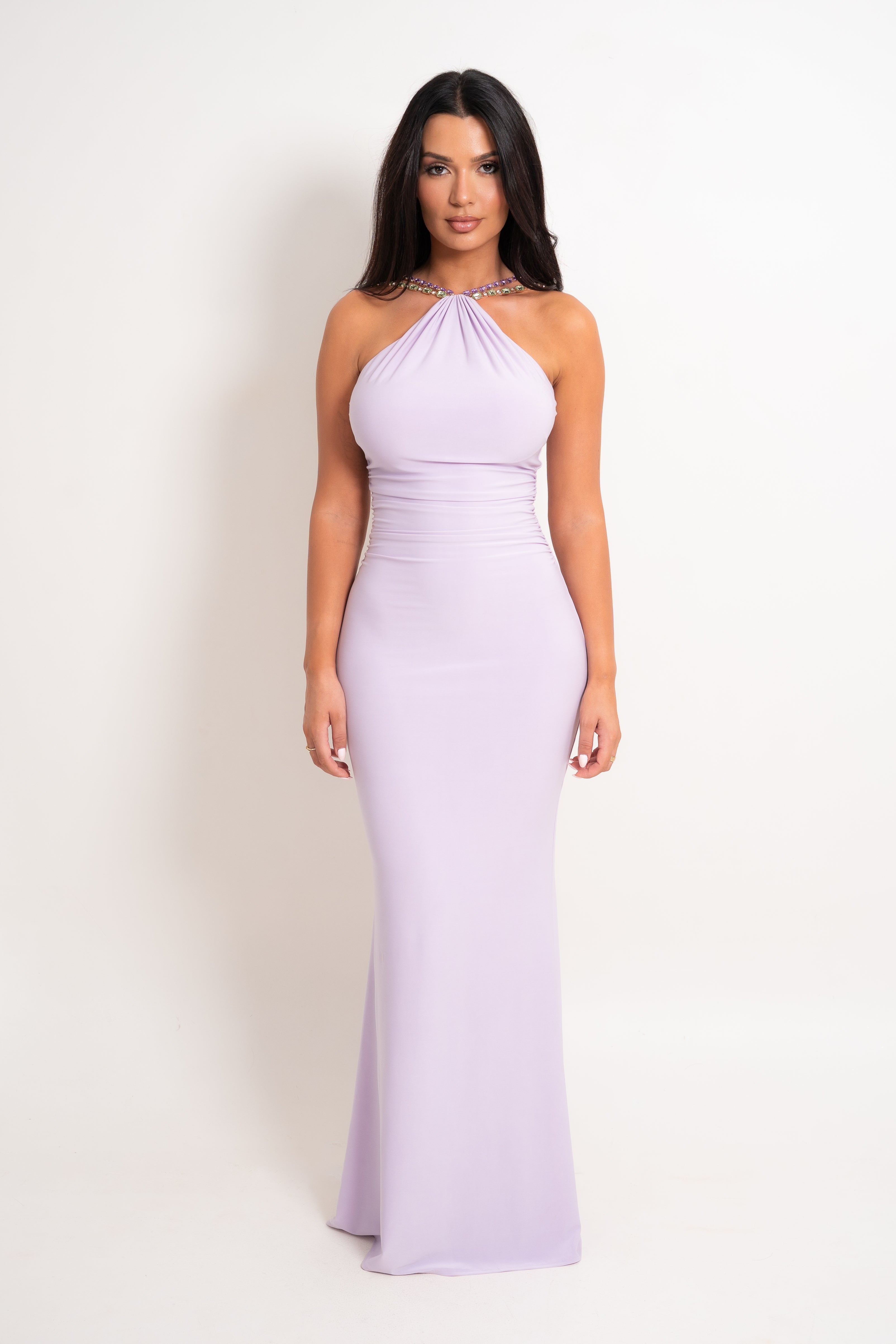 A woman modeling a lavender halter-neck floor-length gown with a fitted bodice and slight flare at the hem, photographed against a plain light background.