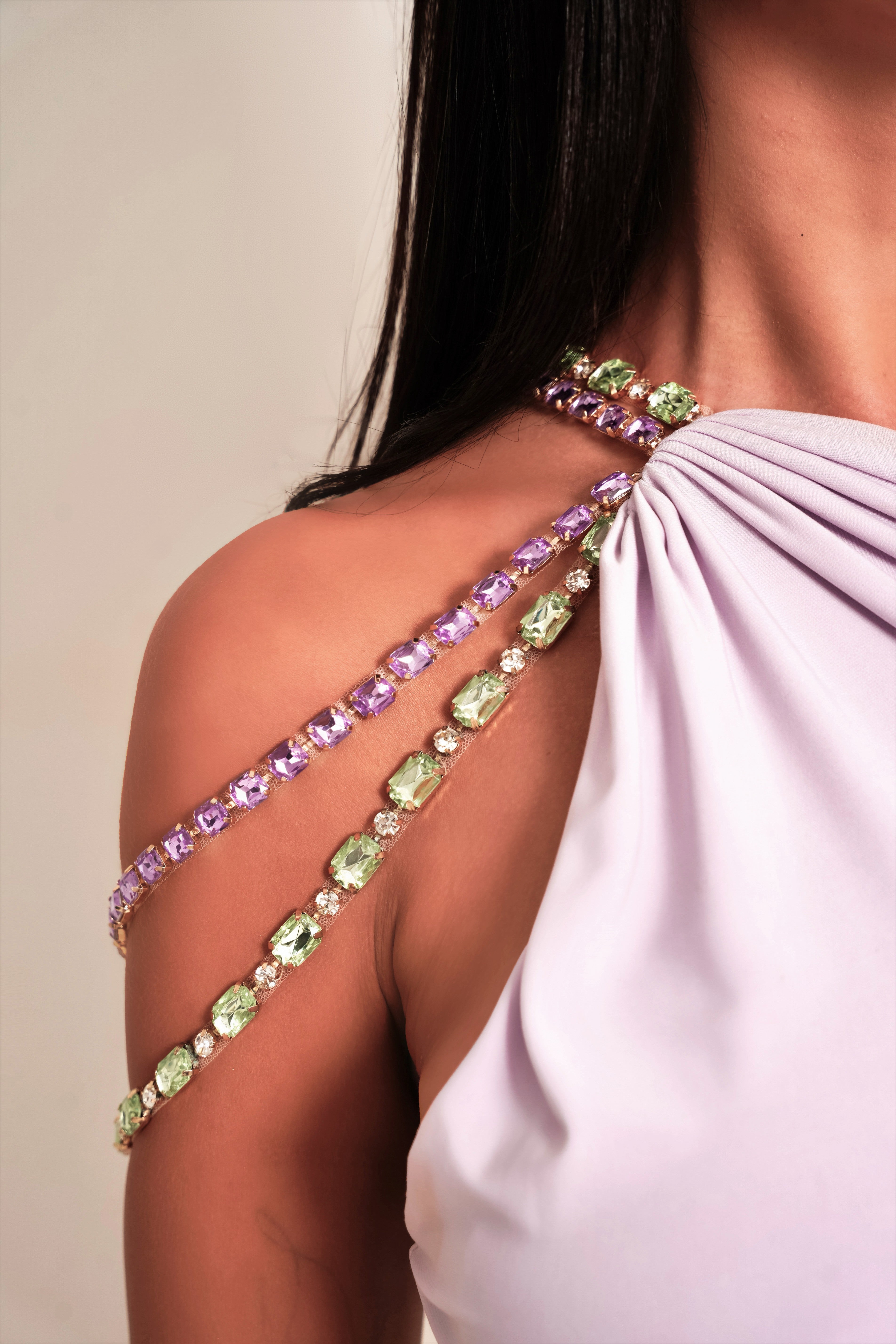 A close-up of a model wearing a light lavender halter top with decorative crystal-embellished shoulder straps in purple and light green.