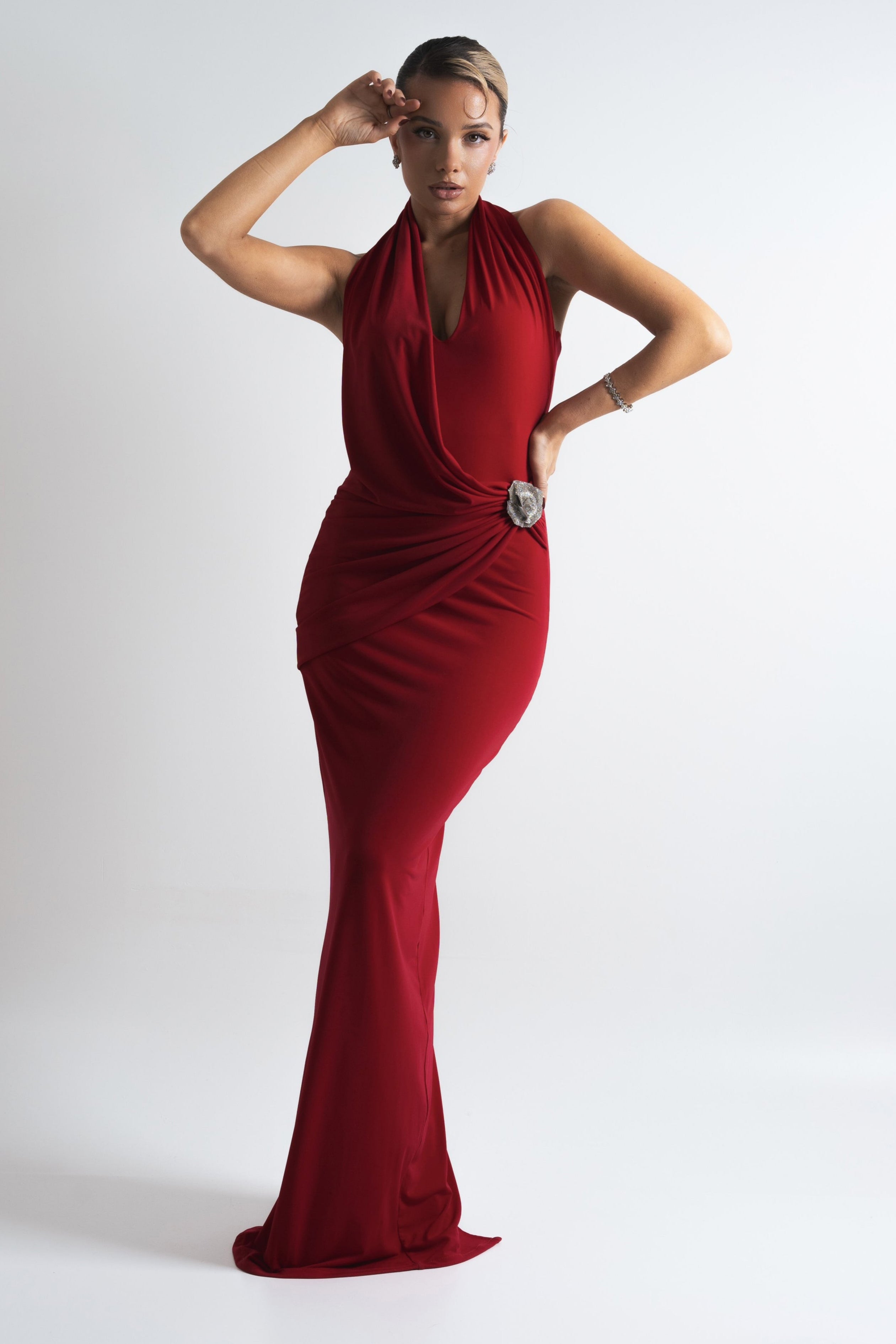 Sophisticated red gown with a sleek silhouette, halter neckline, and a glittering brooch accent for added glamour.