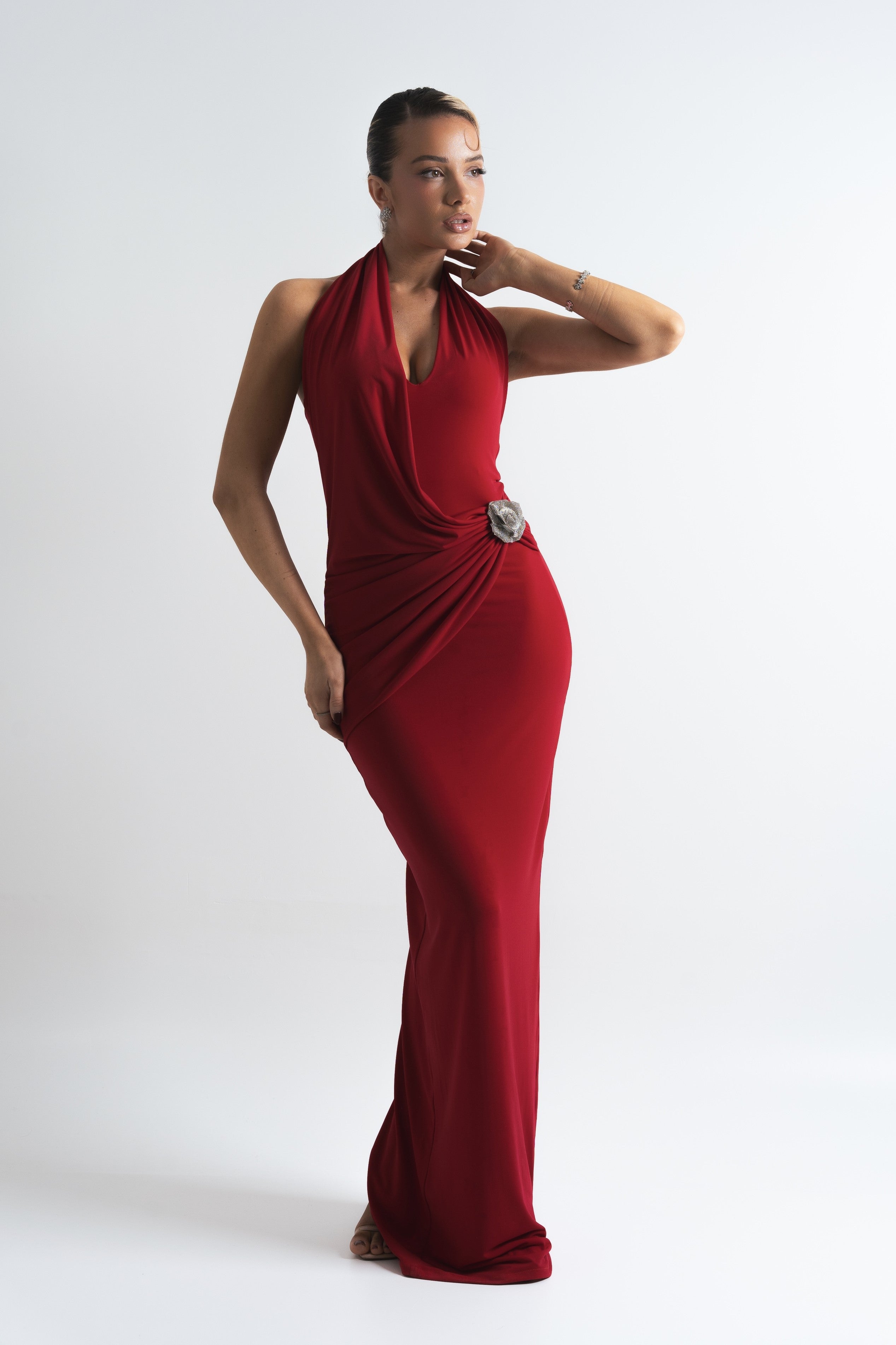 Elegant red maxi dress with a ruched waist, detailed with a crystal brooch, ideal for making a dramatic entrance.