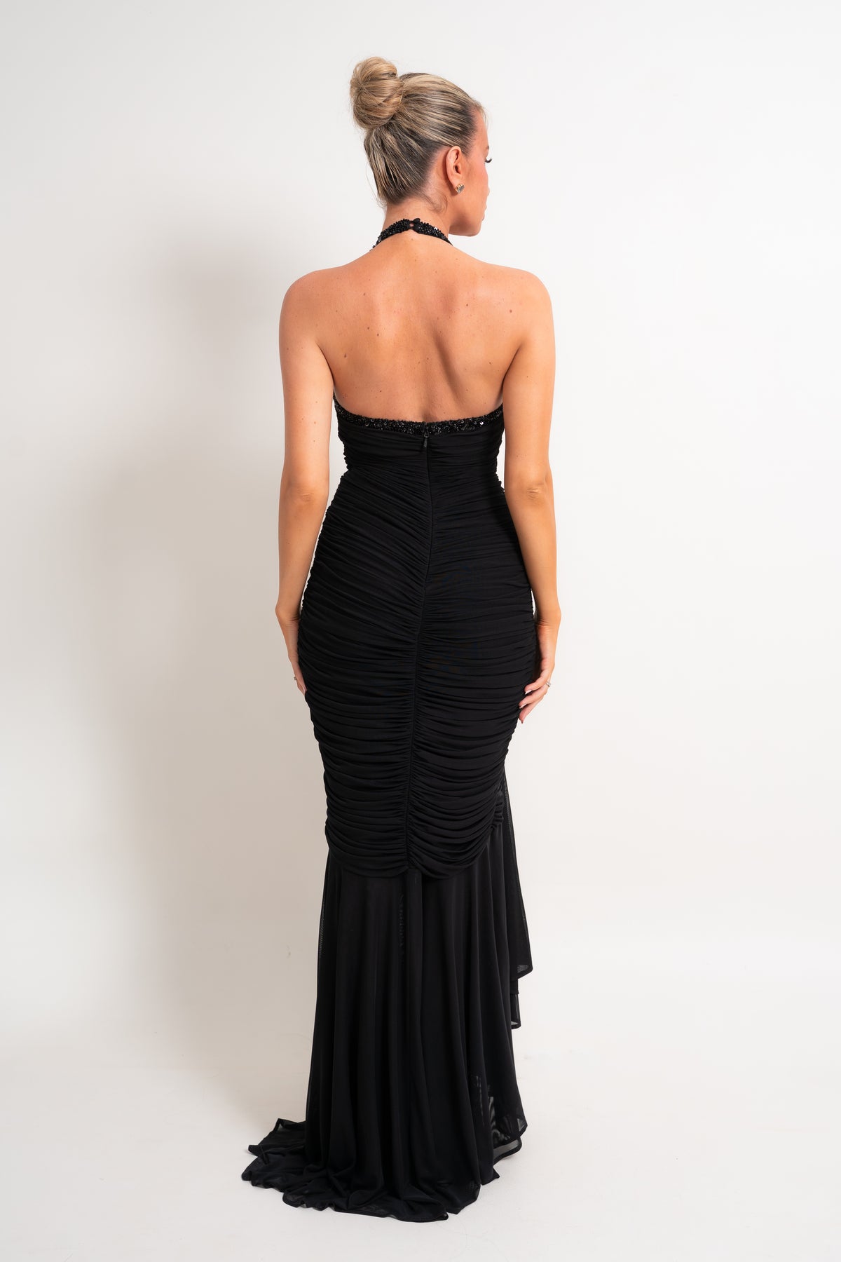 A woman wearing a black strapless ruched mermaid gown, shown from the back against a plain white studio background.
