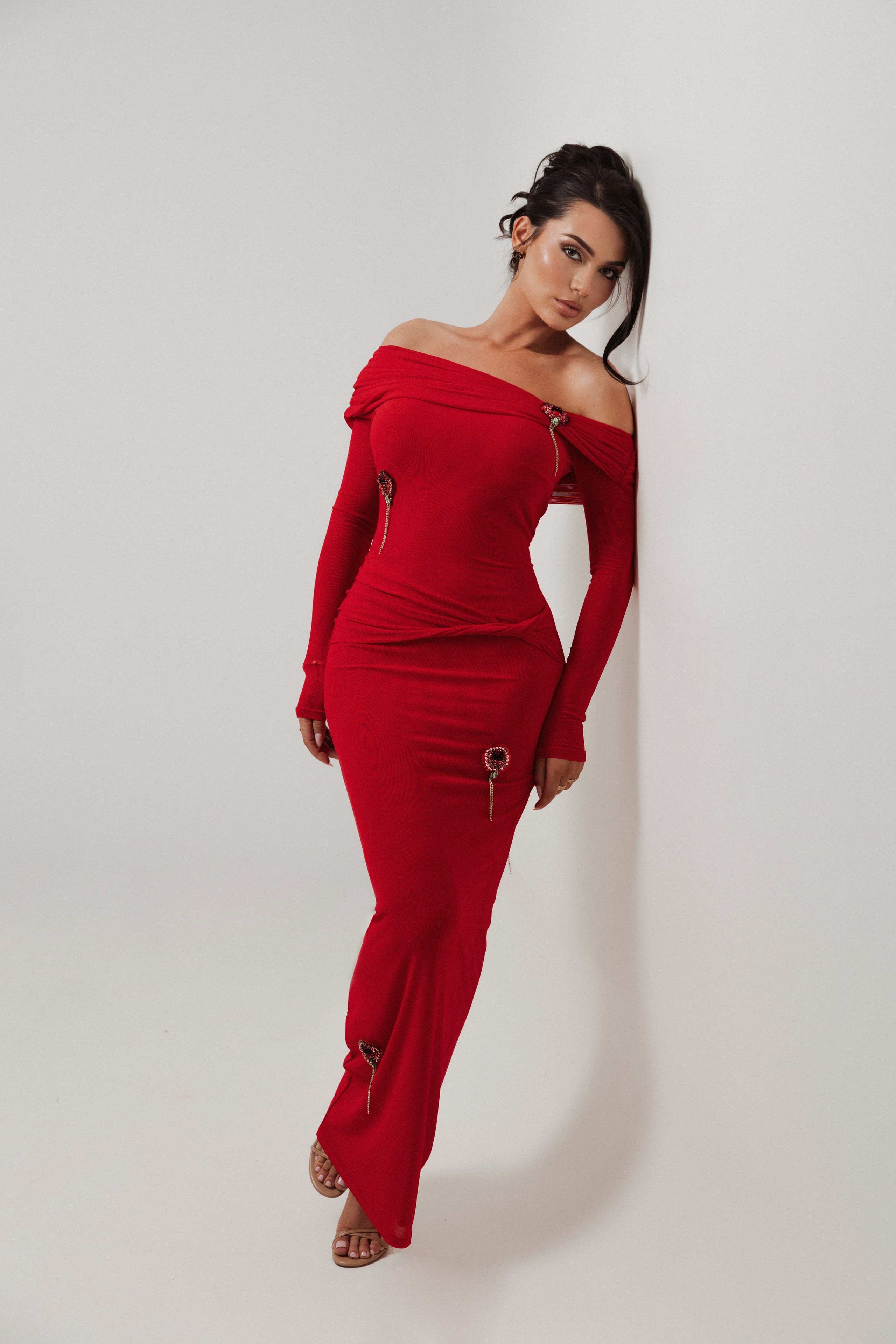 Woman wearing a red off-shoulder jumpsuit against a white background