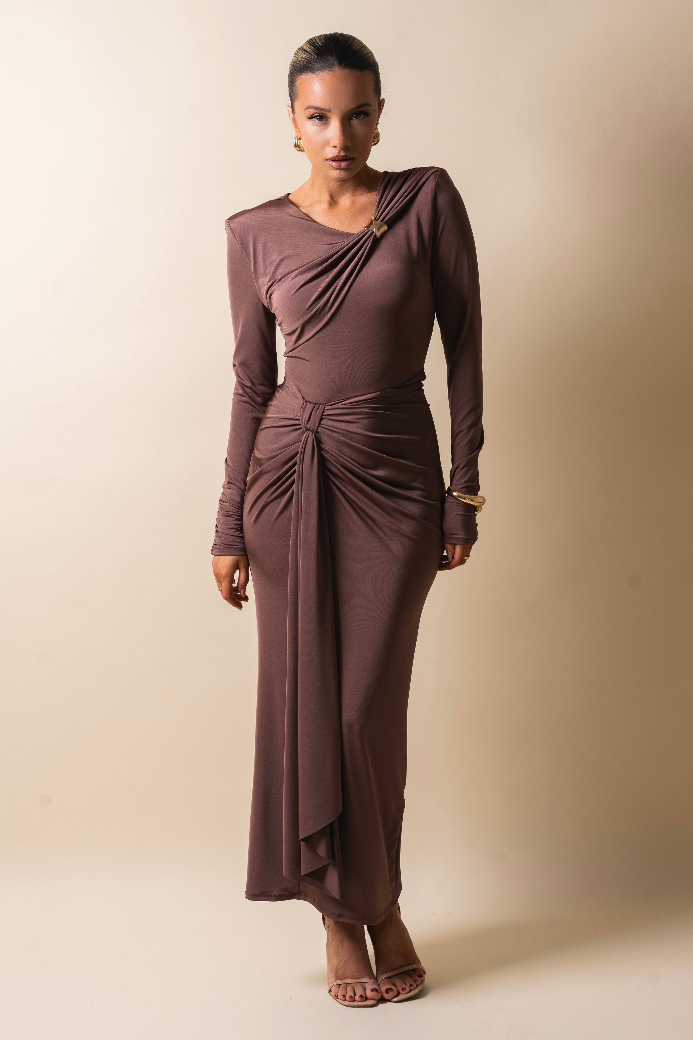 Model wearing a brown one-shoulder dress with a twisted waist and elegant design.