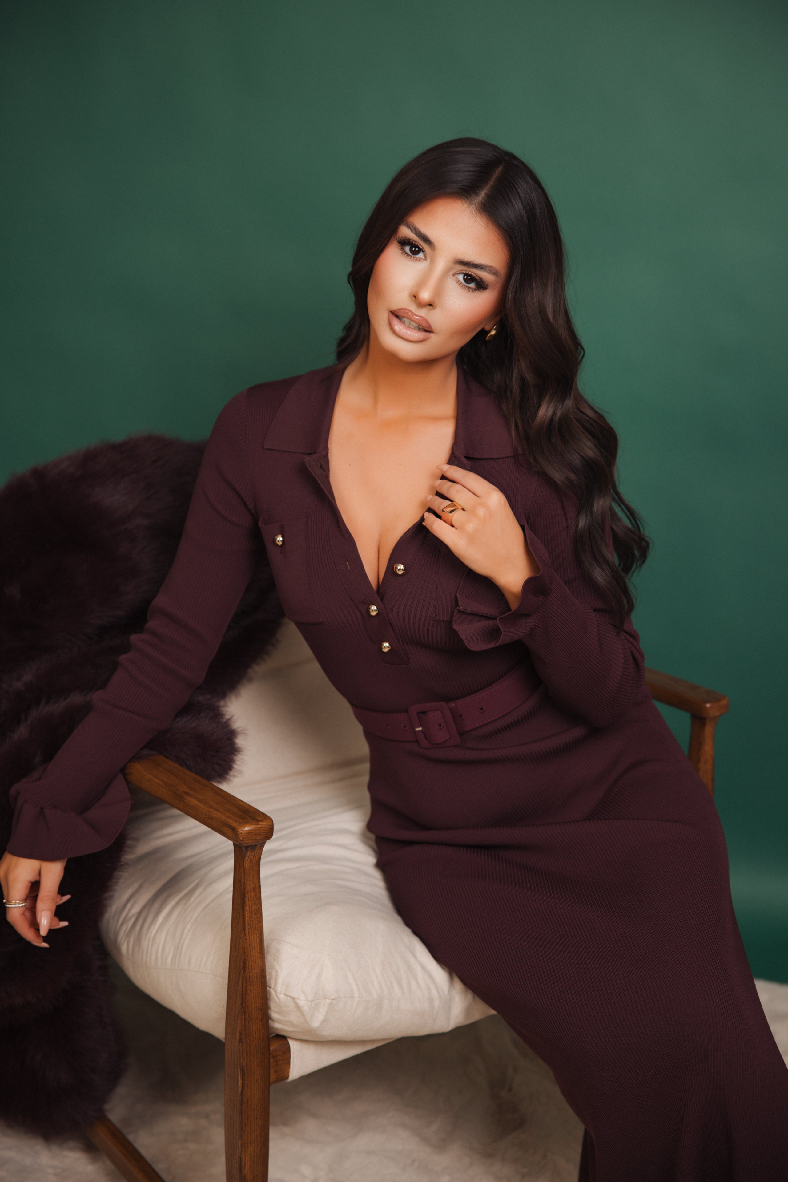 Woman in a dark purple dress sitting on a chair against a green background