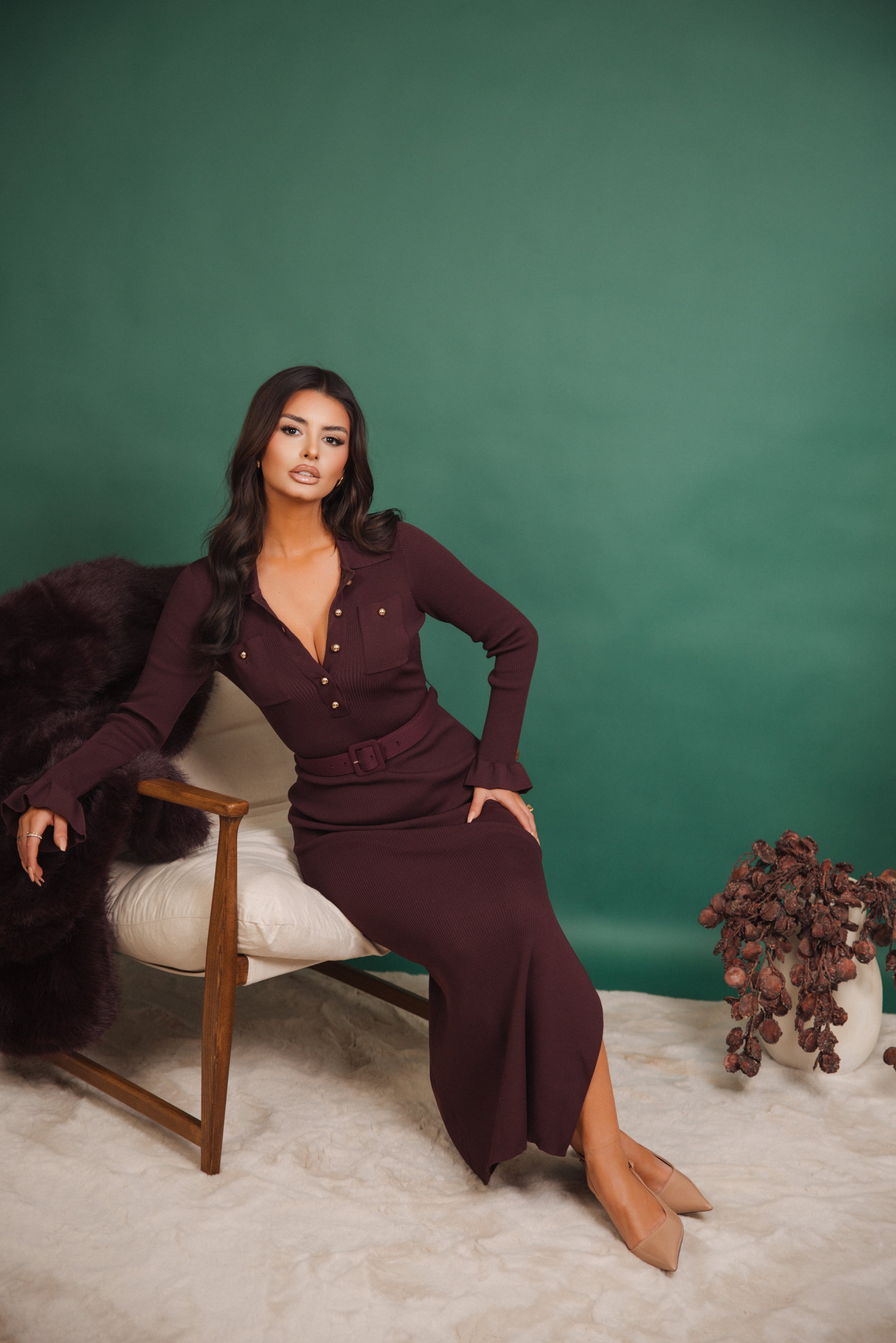 Woman in a burgundy dress sitting on a chair against a green background