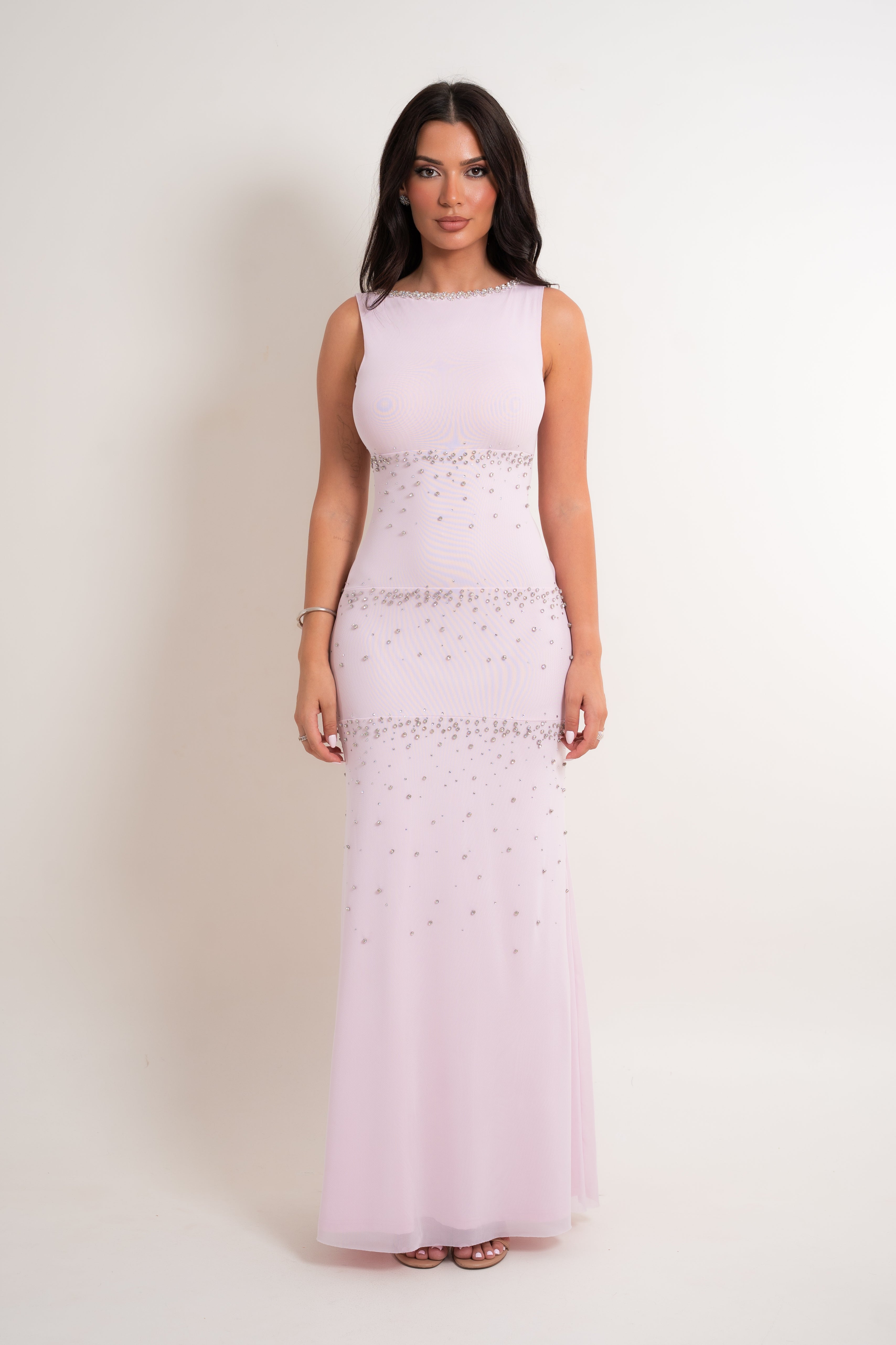 A woman modeling a sleeveless light pink floor-length gown with silver beaded embellishments at the waist and hips, standing against a plain off-white studio background.
